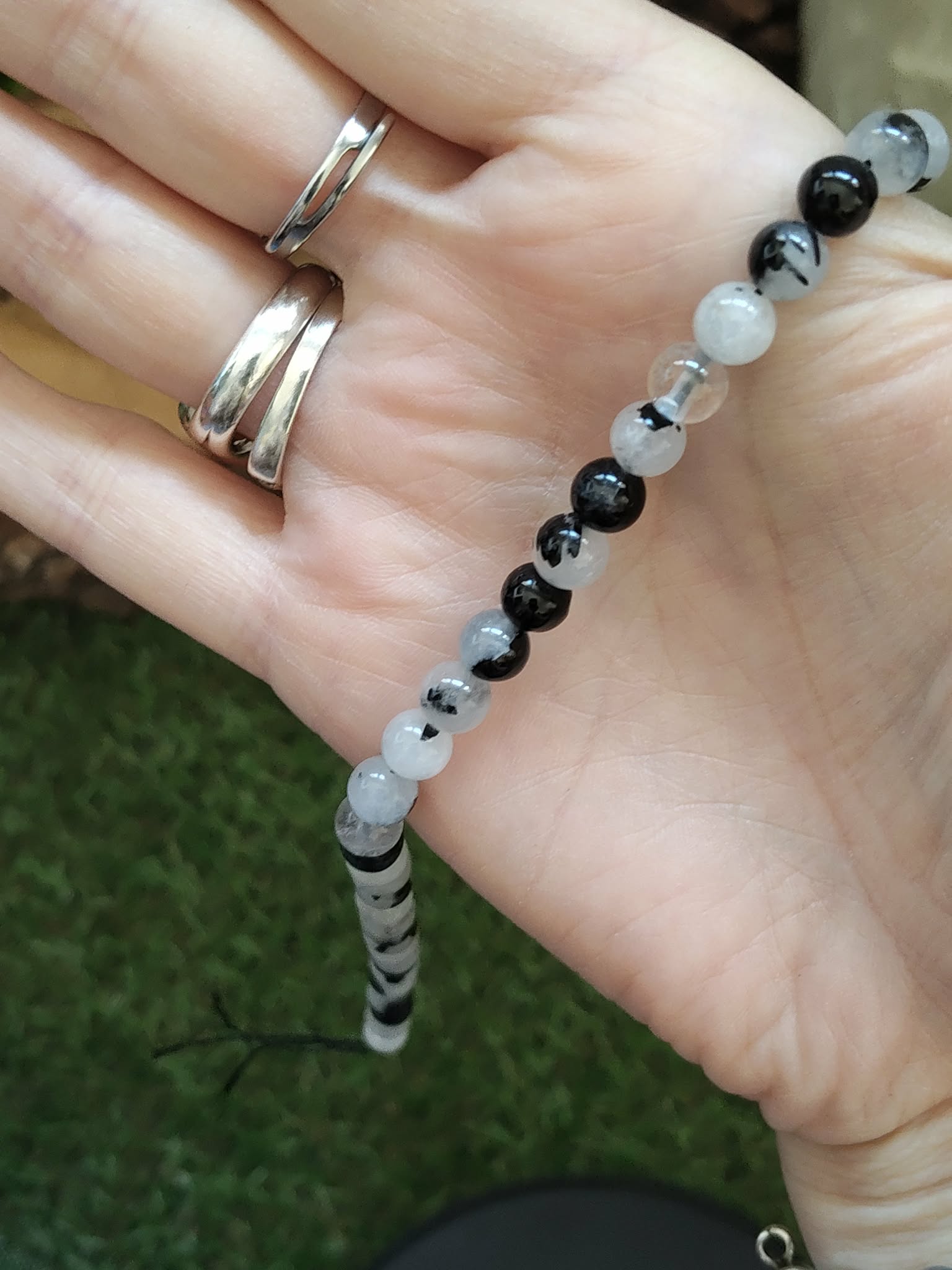 Fil de perles Tourmaline noire et Quartz tourmaliné présenté dans la main, détail des perles 6 mm associées à l’ancrage et au recentrage.