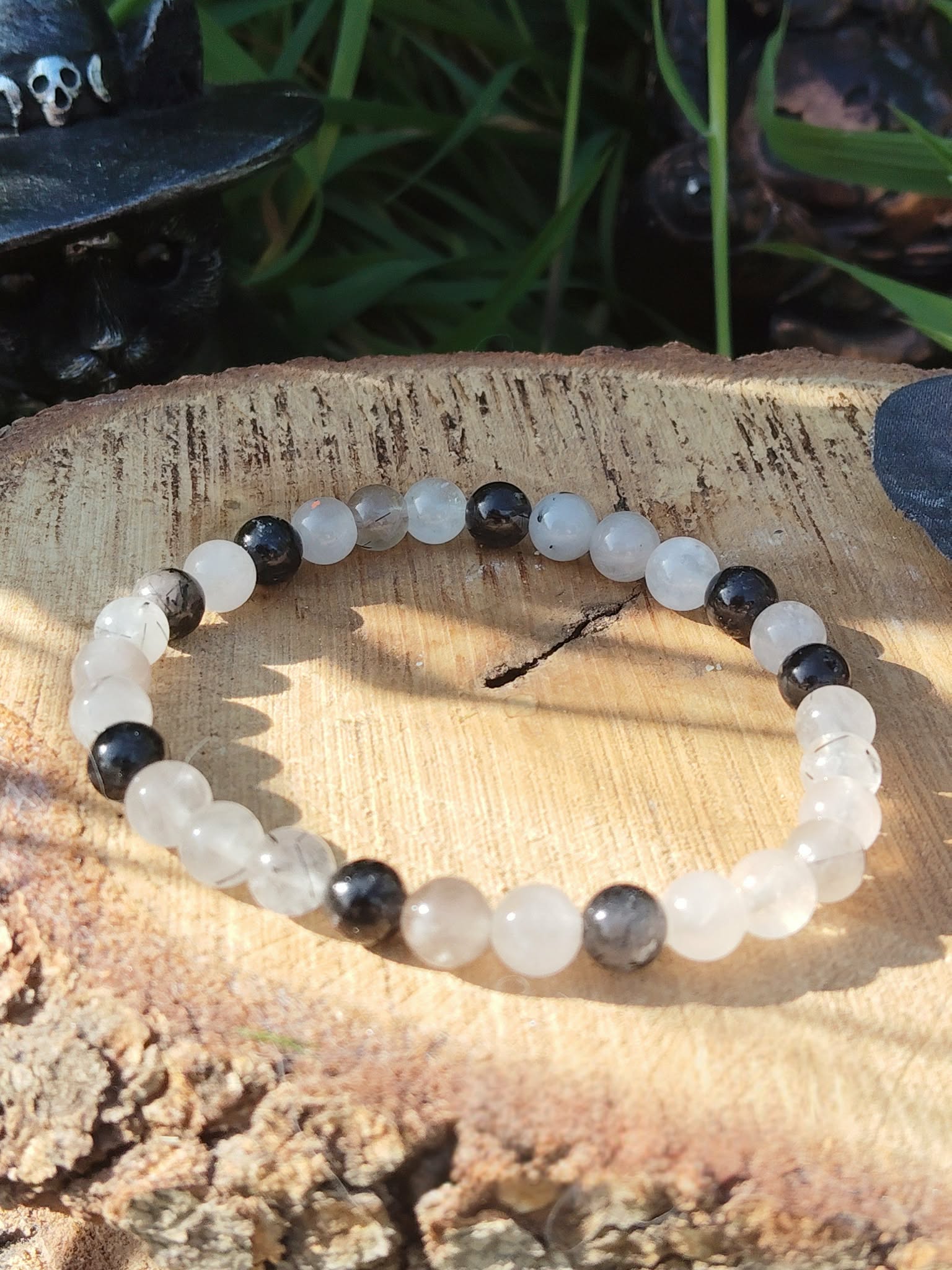Bracelet Tourmaline noire et Quartz tourmaliné 6 mm sur rondin de bois, décor nature avec herbes, protection énergétique et ancrage.