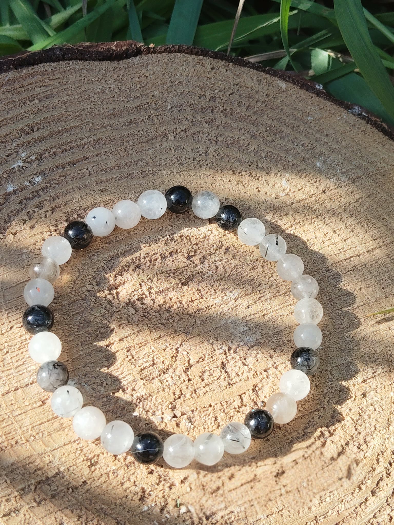 Bracelet Tourmaline noire et Quartz tourmaliné posé sur coupe de bois, perles translucides à inclusions noires pour stabilité et apaisement.