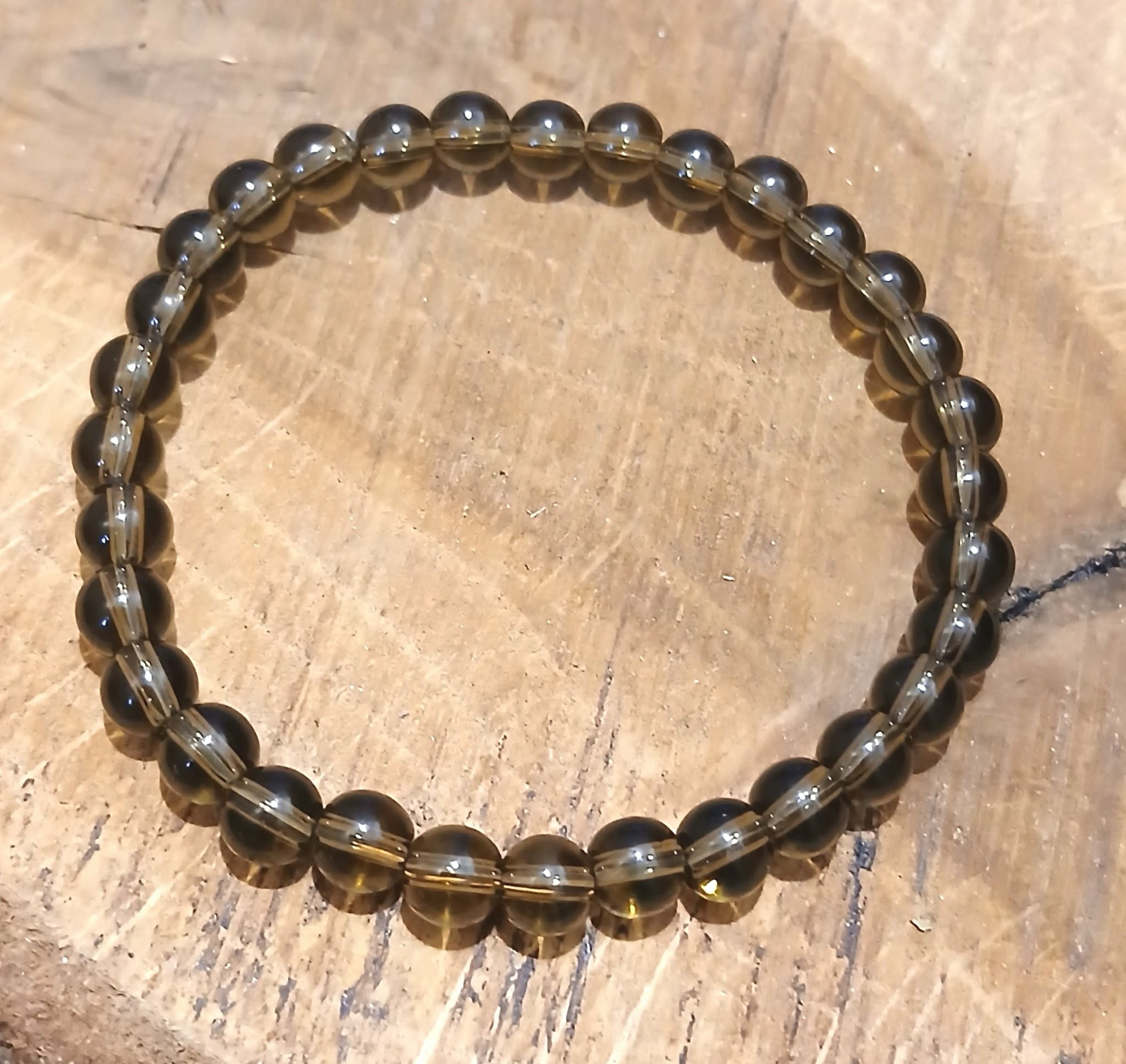 Bracelet en Quartz fumé posé sur bois clair, perles naturelles brun fumé lumineuses, stabilité intérieure et protection énergétique.