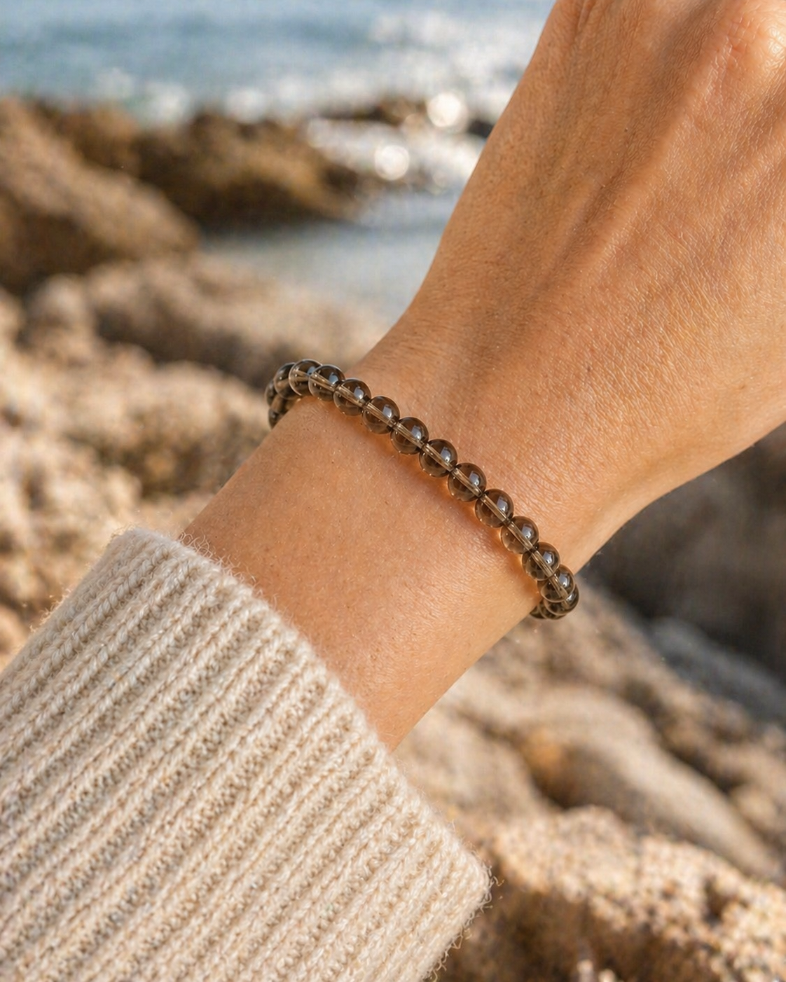 Bracelet Quartz fumé porté au poignet en Bretagne, décor marin flouté, perles brunes translucides pour ancrage et apaisement.