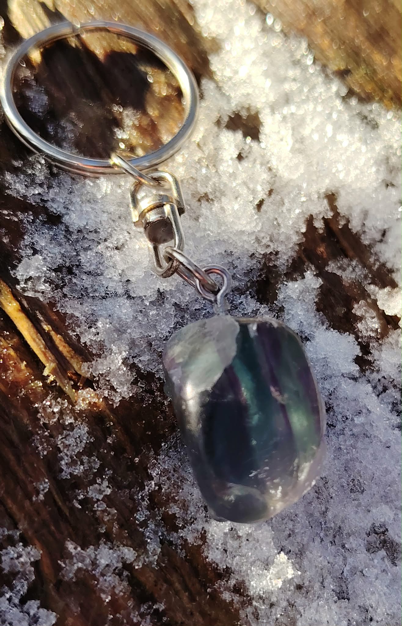 Gros plan sur porte-clés Fluorite multicolore, pierre polie aux nuances vertes et violettes sur fond naturel.