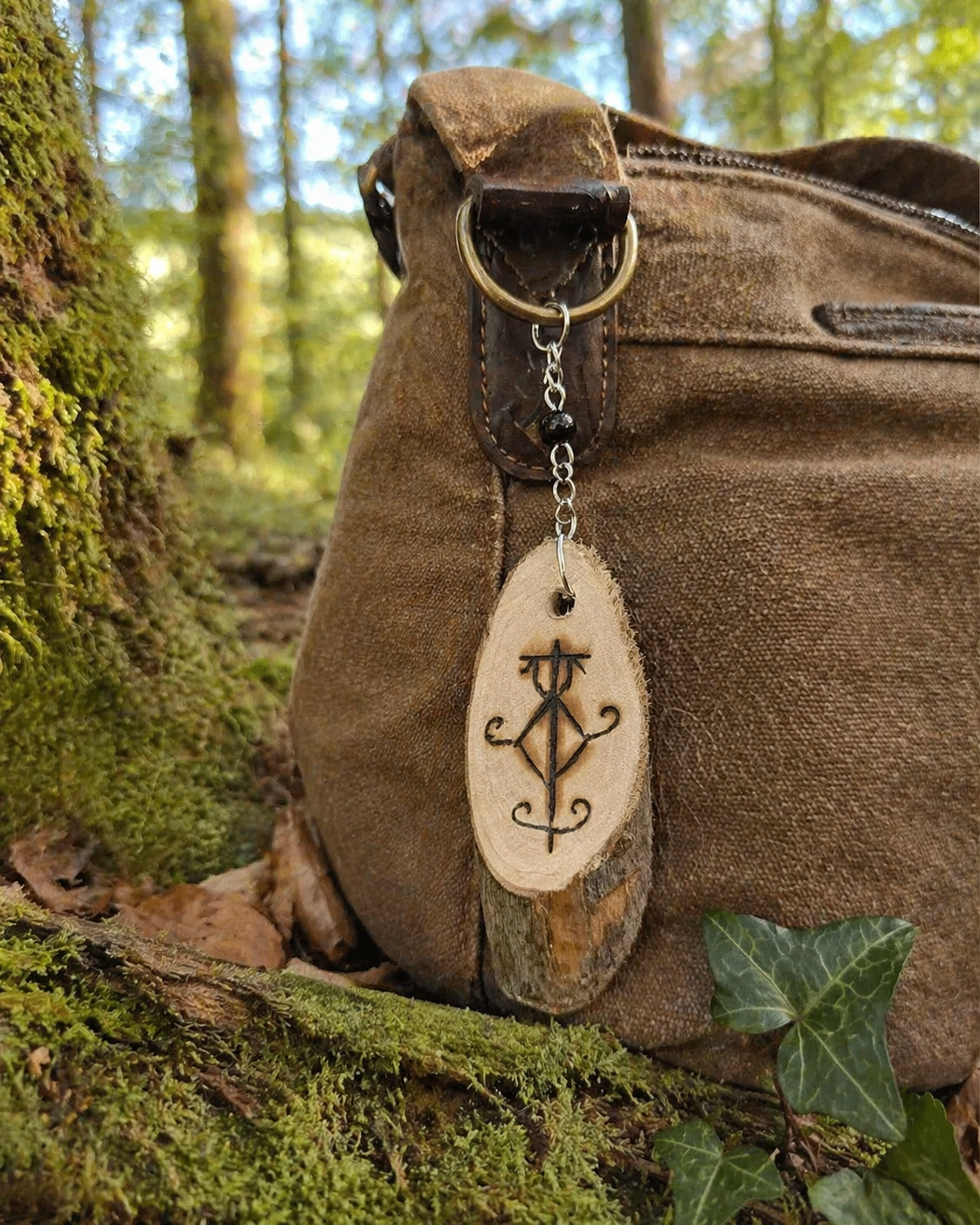 Bijou de sac Sigile de Protection Physique accroché à un sac brun en forêt, avec bois gravé et Tourmaline noire d’ancrage.