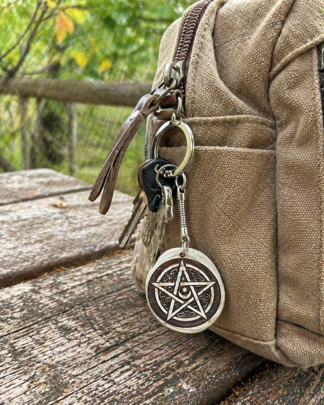 Porte clés pentacle en bois accroché à un sac beige en extérieur, mise en situation naturelle pour harmonie et recentrage.