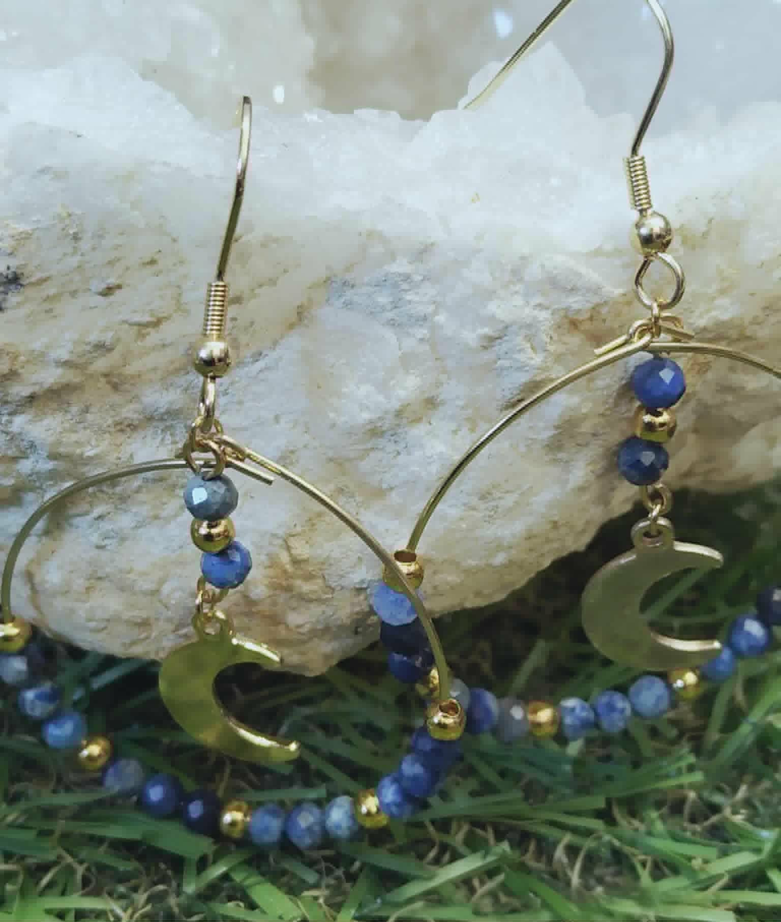 Boucles d’oreilles lapis lazuli facetté posées près d’une pierre claire, créoles dorées avec lunes pour clarté et expression de soi.