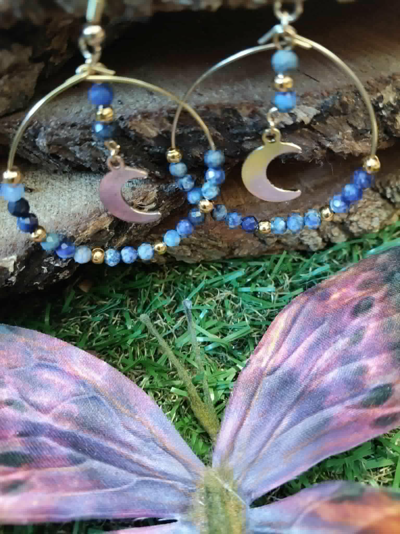 Boucles d’oreilles lune en lapis lazuli sur décor naturel avec papillon violet, création Magic Gaïa pour harmonie intérieure.
