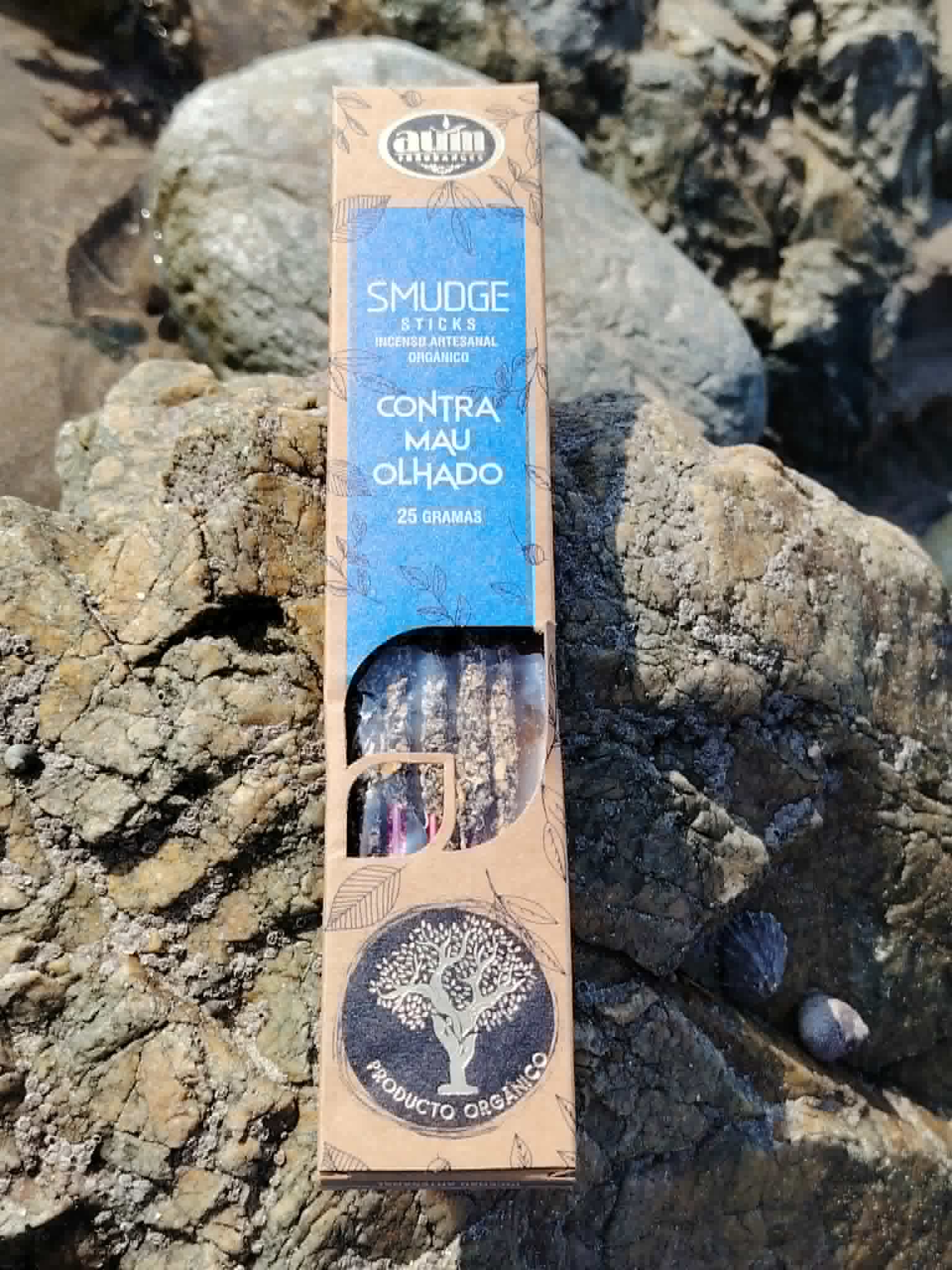 Encens organique AUM Contra Mau Olhado 25 g en situation sur roche, avec décor marin breton et intention de protection douce.