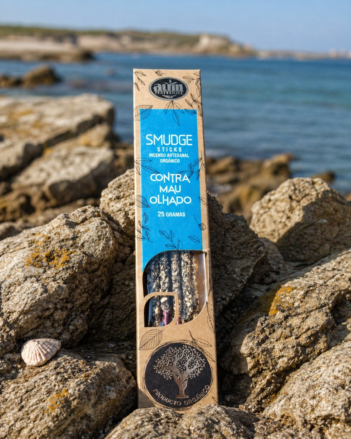 Encens AUM Organico Contre le Mauvais Œil 25 g posé sur roche en bord de mer breton, boîte kraft et bleue avec bâtonnets visibles.
