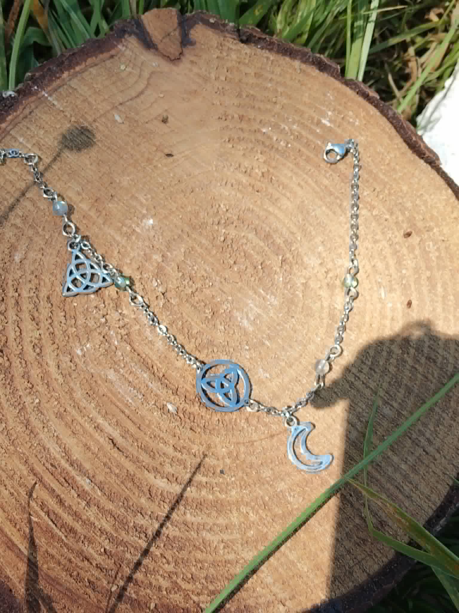 Chaîne de cheville triquetra et lune en acier inoxydable argenté, avec perles de labradorite et aqua aura 4 mm sur décor naturel.