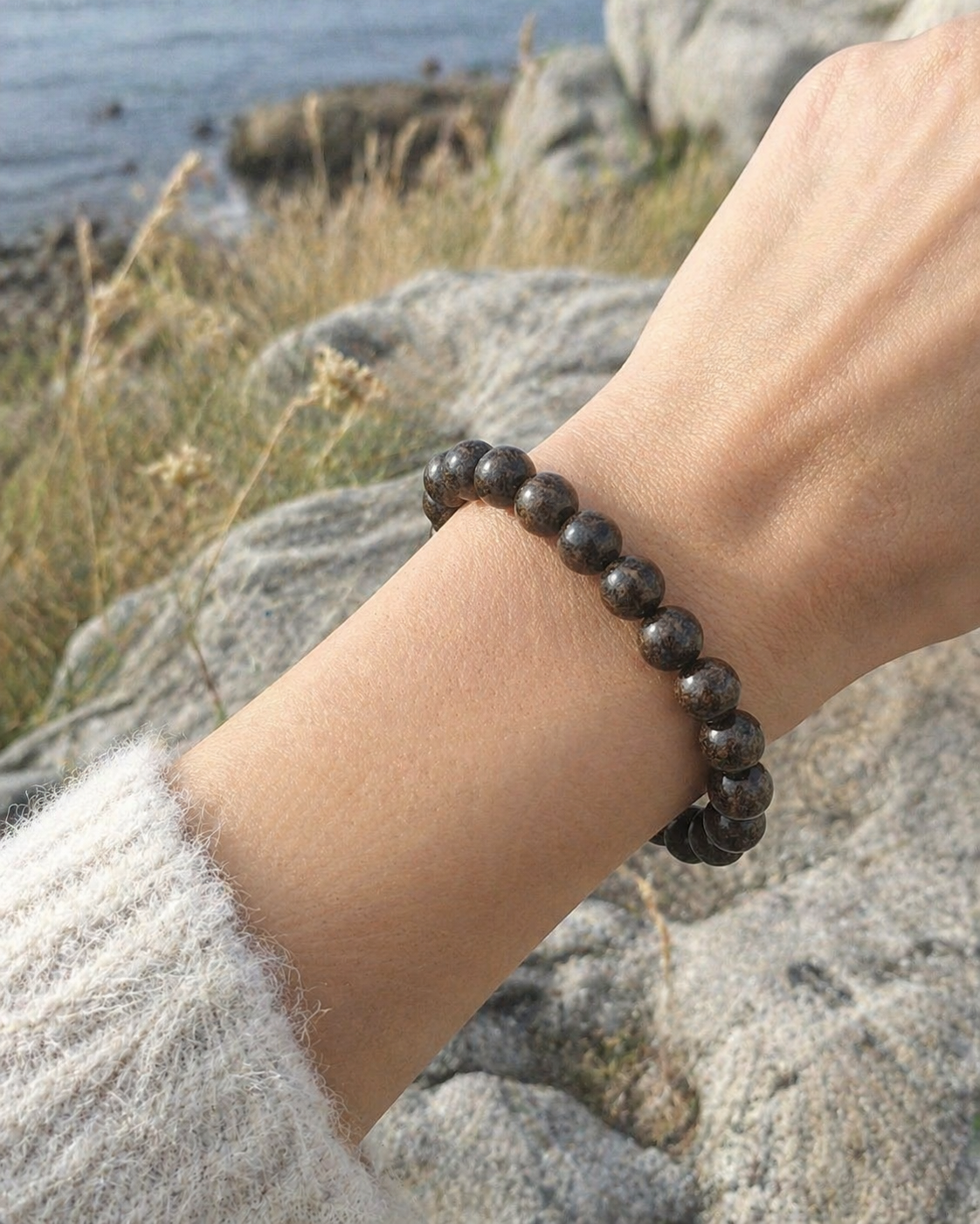 Bracelet bronzite porté au poignet en décor naturel breton, perles sombres et dorées pour ancrage, courage et protection symbolique.