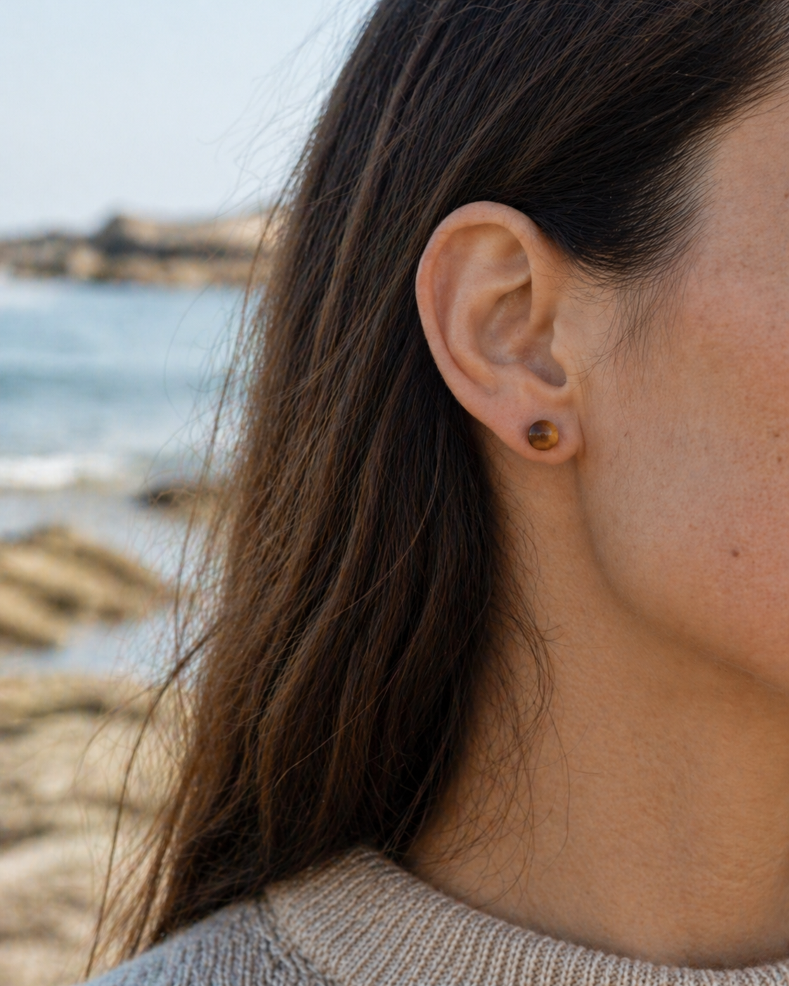 Puces d’oreilles œil de tigre portées en décor marin breton, petites perles 6 mm aux nuances miel et brun chaud.