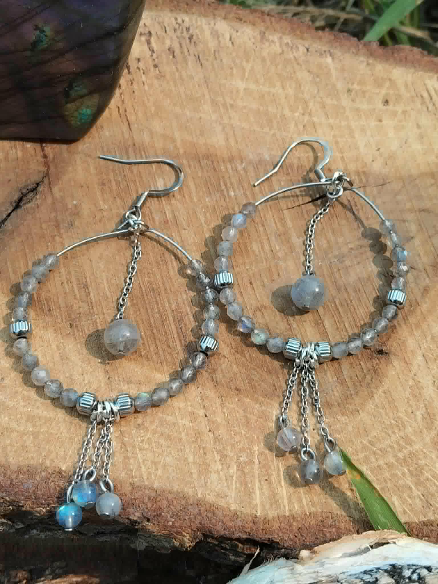 Créoles labradorite argentées posées sur tranche de bois, chaîne centrale et perles grises pour intuition et protection symbolique.