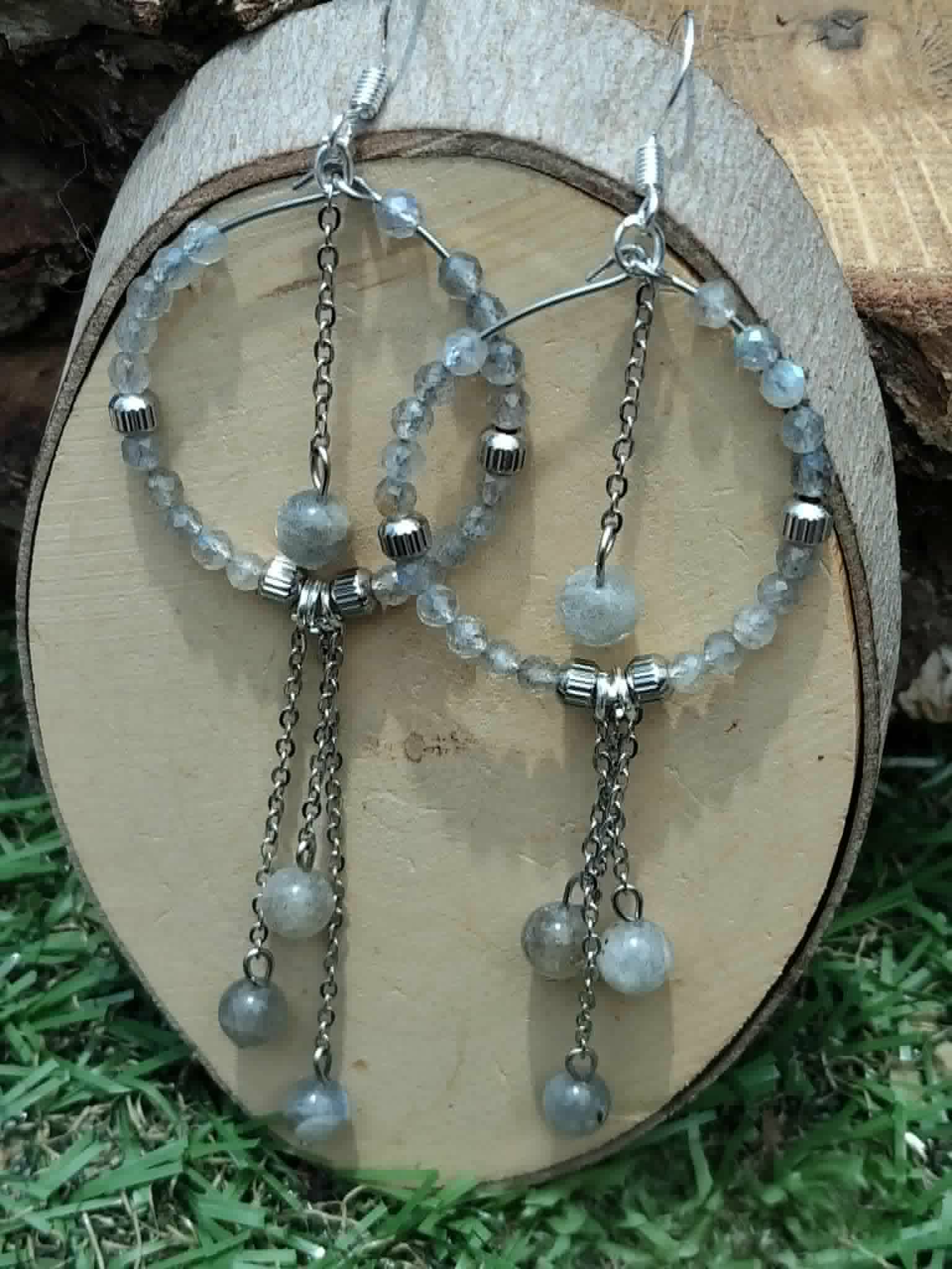 Boucles créoles labradorite argentées sur rondin de bois et herbe, longues chaînes mobiles et reflets gris bleutés apaisants.