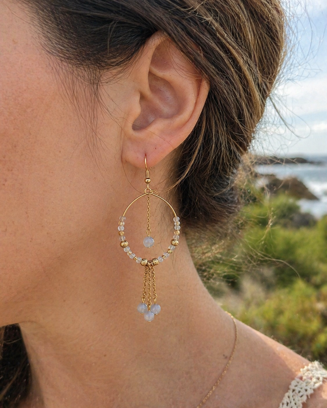 Version dorée des créoles labradorite portée face à la mer, bijou lumineux avec chaîne centrale pour protection symbolique.