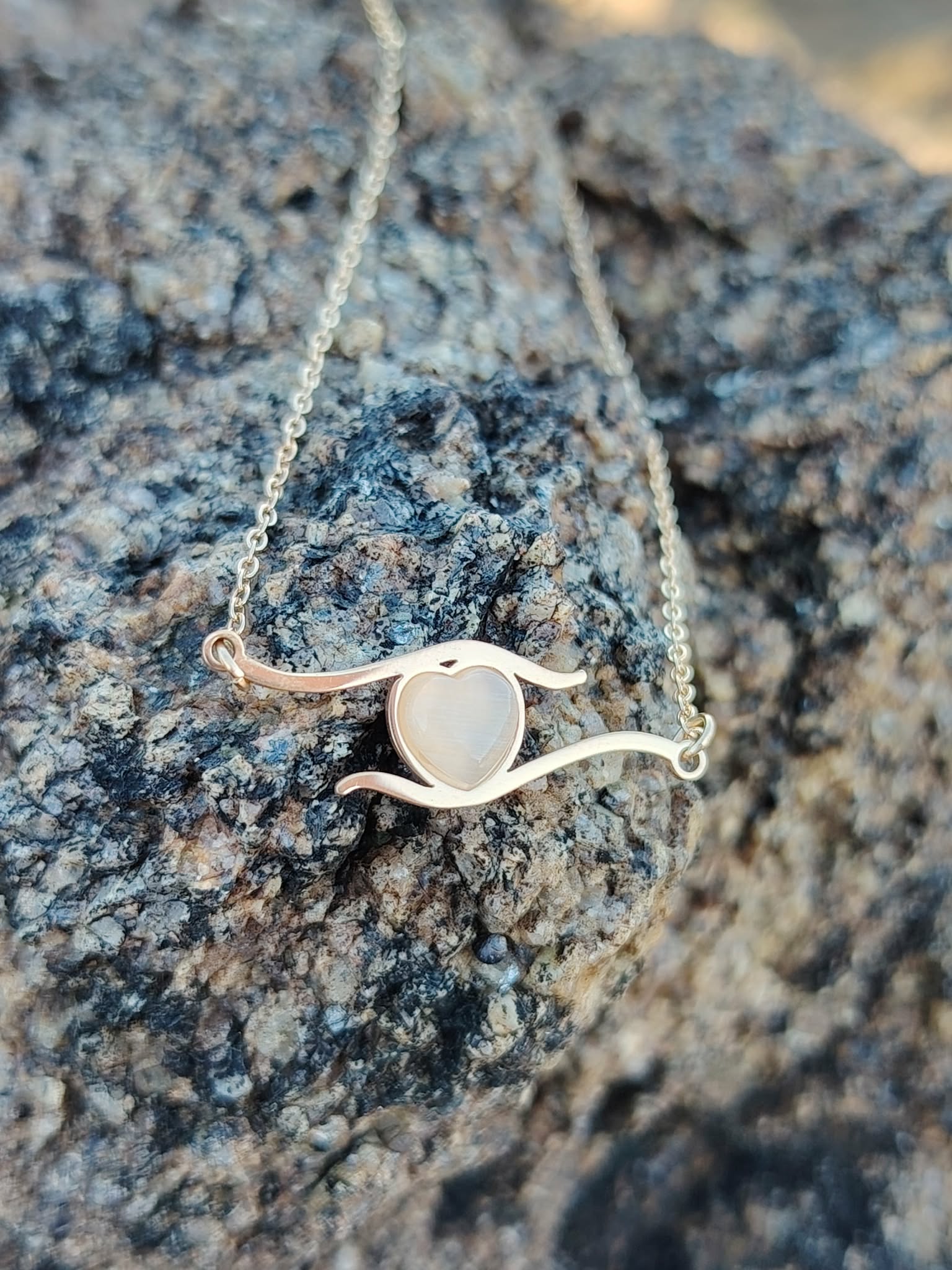 Collier cœur en acier inoxydable doré posé sur roche brute, pendentif clair au centre pour amour de soi et douceur au quotidien.
