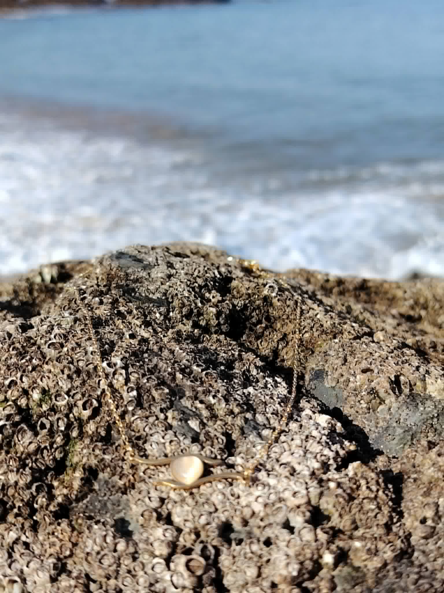 Collier acier inoxydable doré rose posé sur roche face à la mer en Bretagne, petit cœur lumineux pour lien précieux.