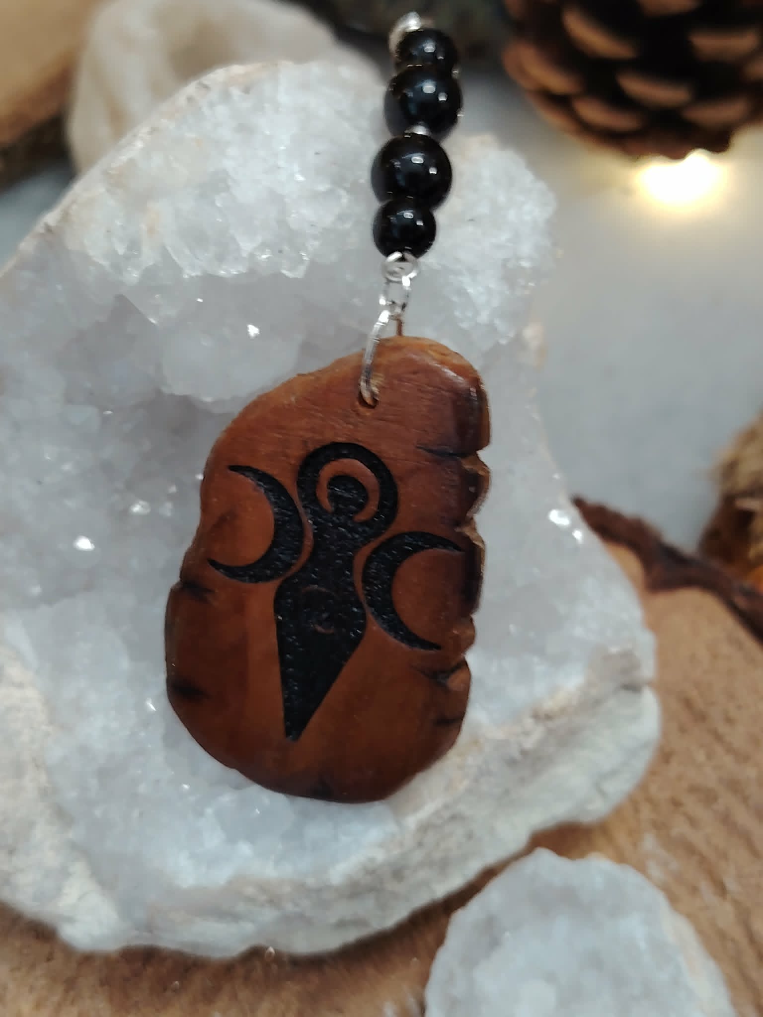 Bijou de rétroviseur Gaïa adossé à un cristal de roche brut, bois pyrogravé et perles noires pour protection symbolique.