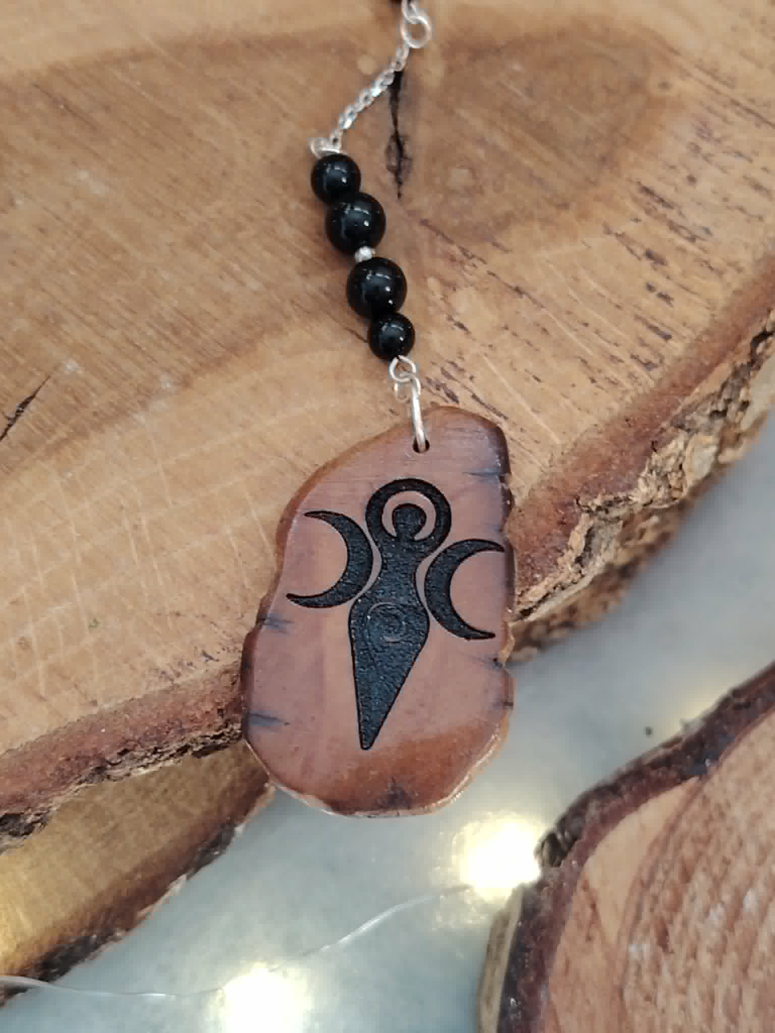 Bijou de rétroviseur en bois face Gaïa sur décor de bois brut, tourmaline noire et chaîne argentée pour une touche mystique.