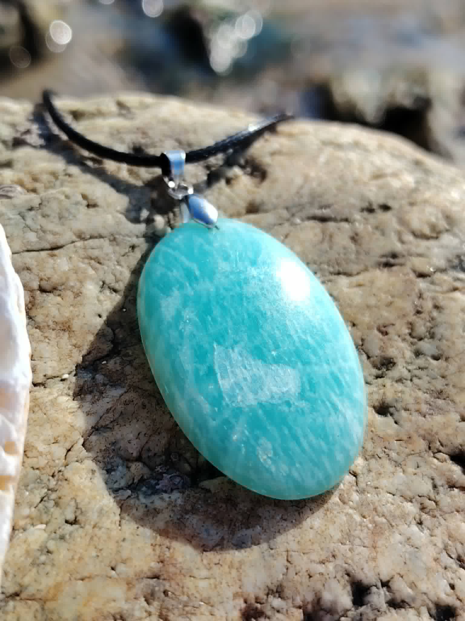 Gros plan du pendentif Amazonite sur roche claire, pierre polie du Pérou pour légèreté émotionnelle et intuition.
