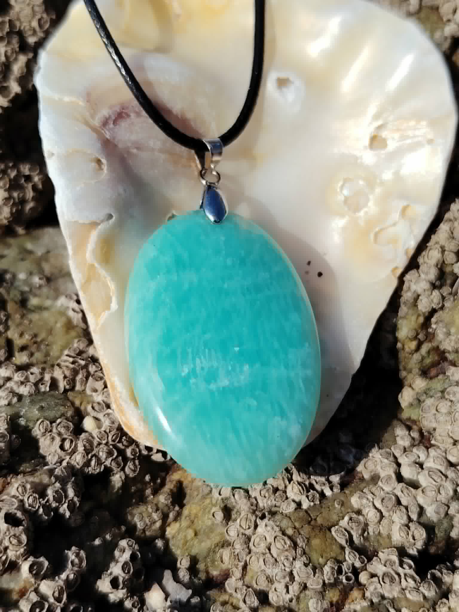 Pendentif Amazonite du Pérou posé sur coquillage en bord de mer, pierre bleu-vert pour douceur et apaisement émotionnel.