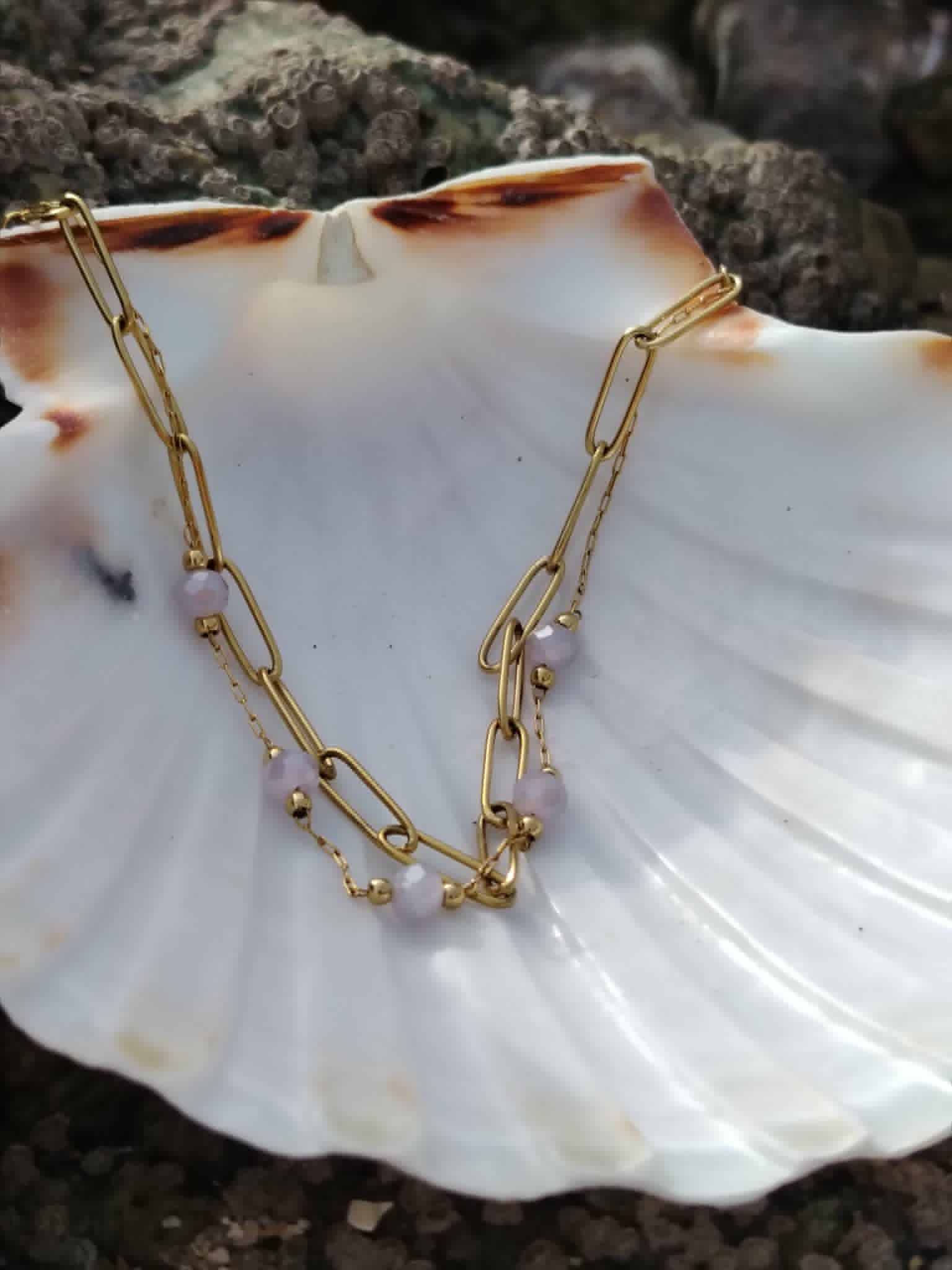 Bracelet fin en acier inoxydable doré présenté sur coquillage nacré, perles facettées violettes et éclat subtil.
