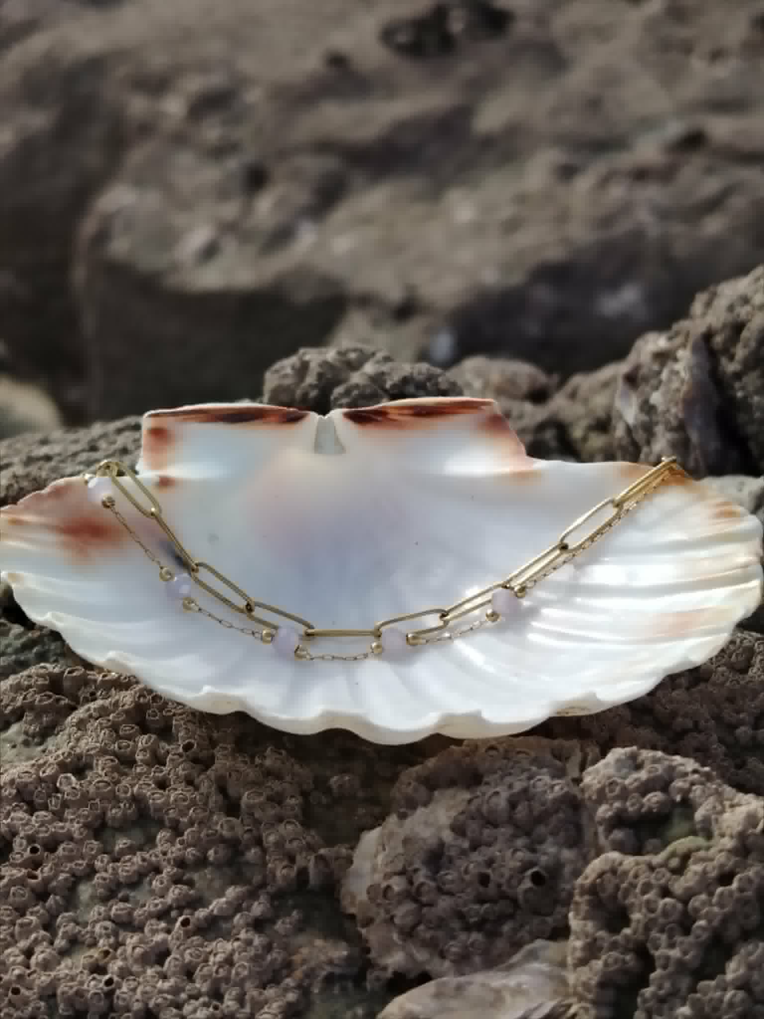 Bracelet acier inoxydable doré dans un grand coquillage blanc, bijou léger aux nuances mauves et style chic.