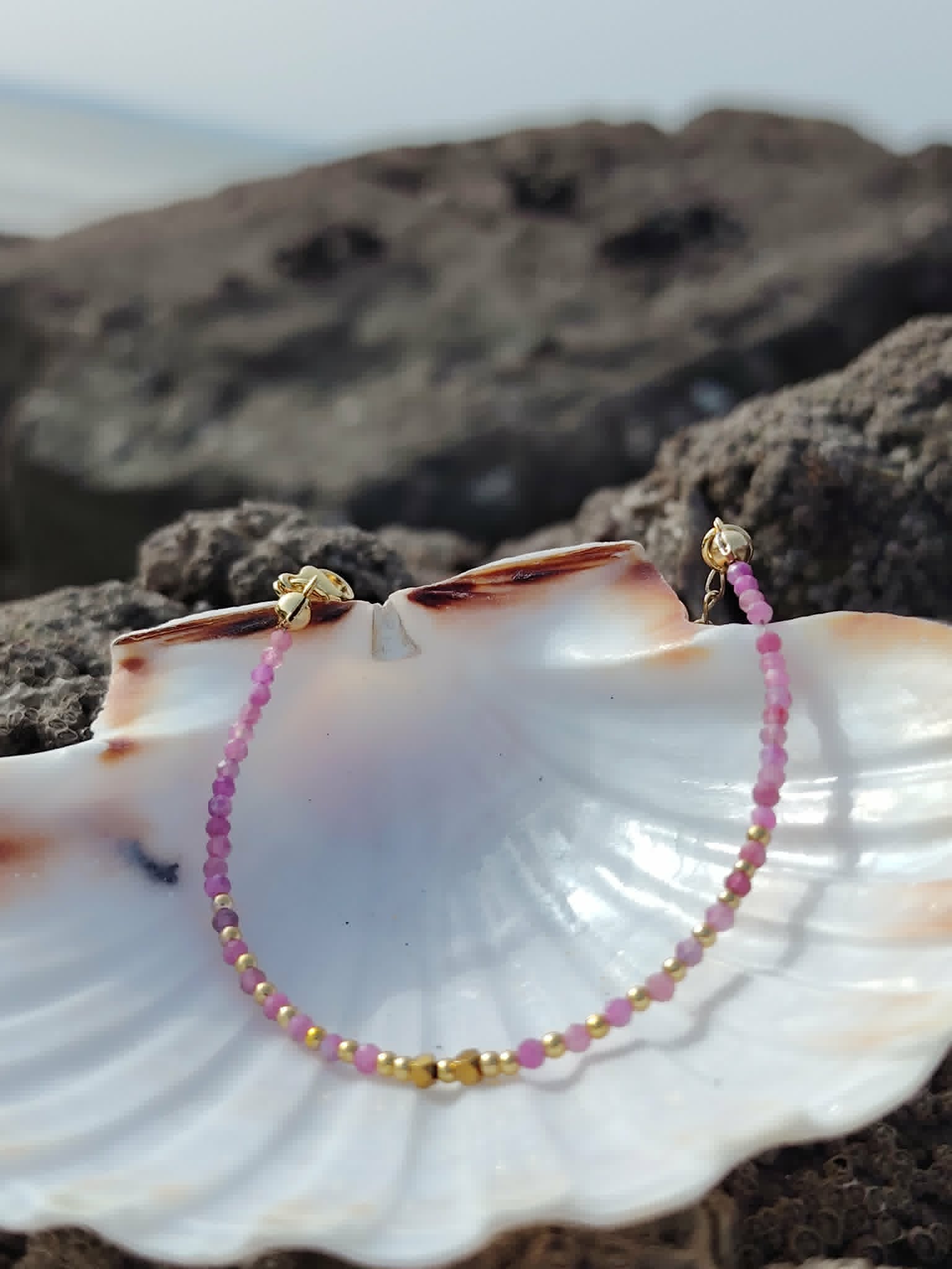 Bracelet Tourmaline rose présenté dans une coquille nacrée en bord de mer, création fine aux nuances poudrées.
