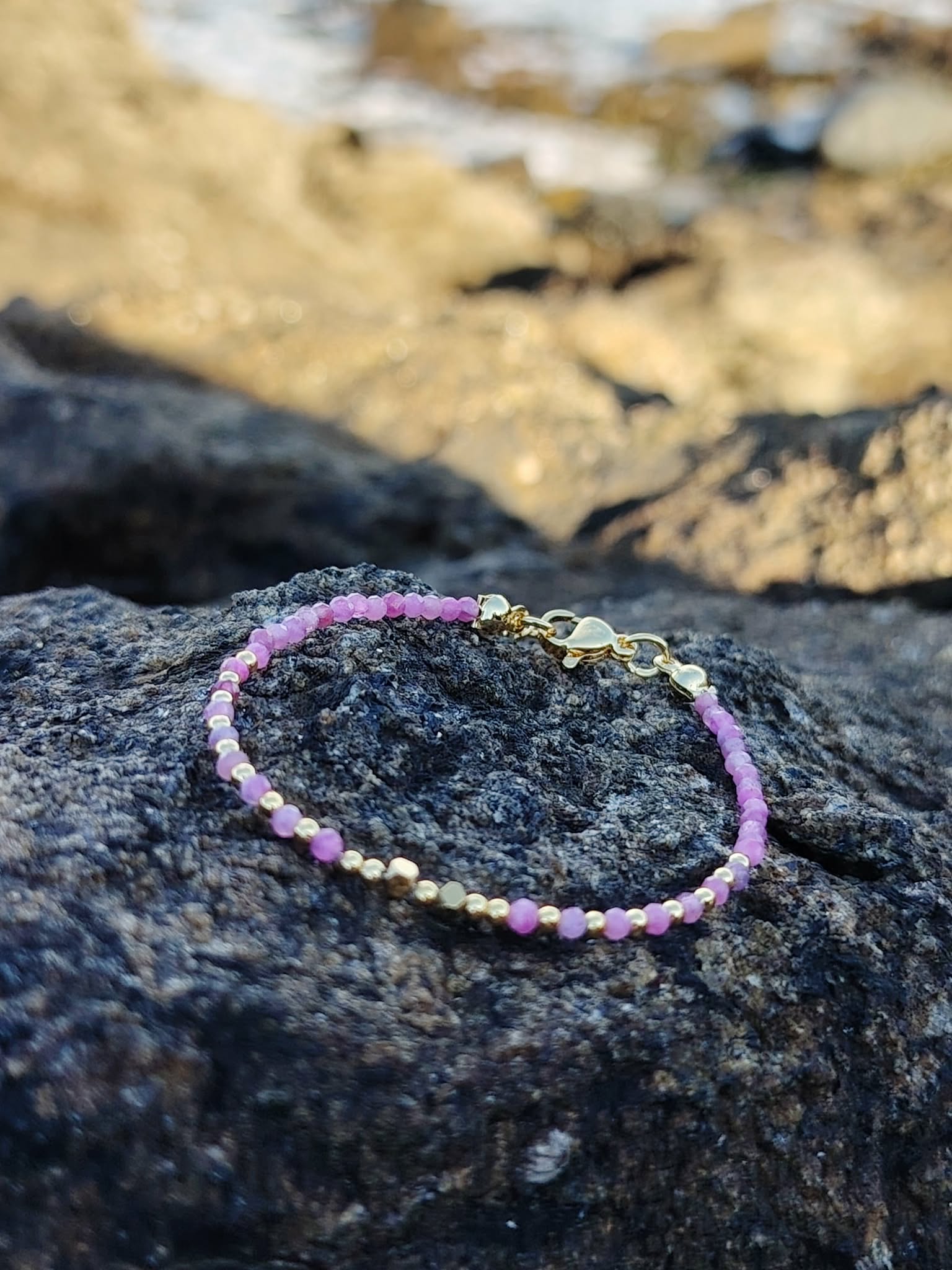 Bracelet en Tourmaline rose facettée sur roche côtière, éclats dorés et perles roses pour équilibre affectif.