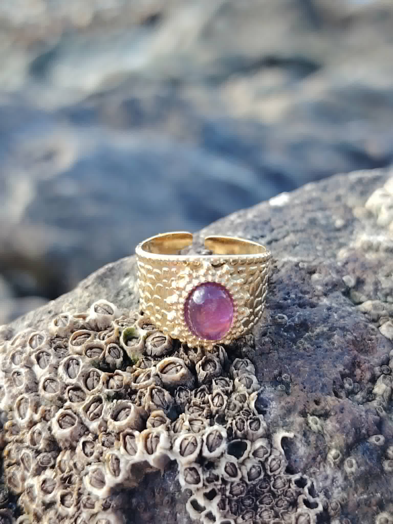 Bague acier inoxydable doré avec Améthyste posée sur roche côtière bretonne, pierre violette pour calme et sérénité.