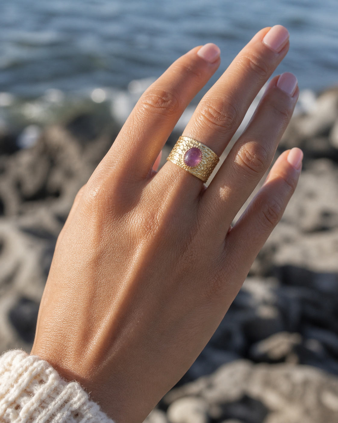 Bague Améthyste portée au doigt face à la mer, bijou doré ajustable au relief martelé pour intuition et élégance.