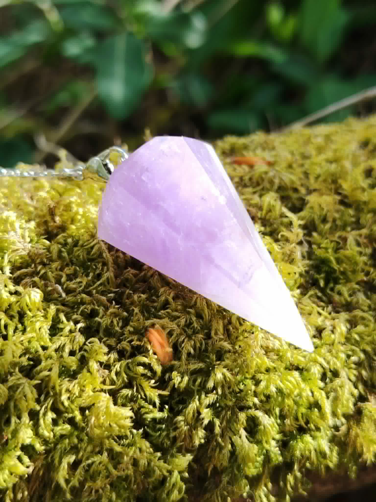Gros plan du pendule Améthyste sur mousse verte, pointe facettée violette pour apaisement et pratiques énergétiques.