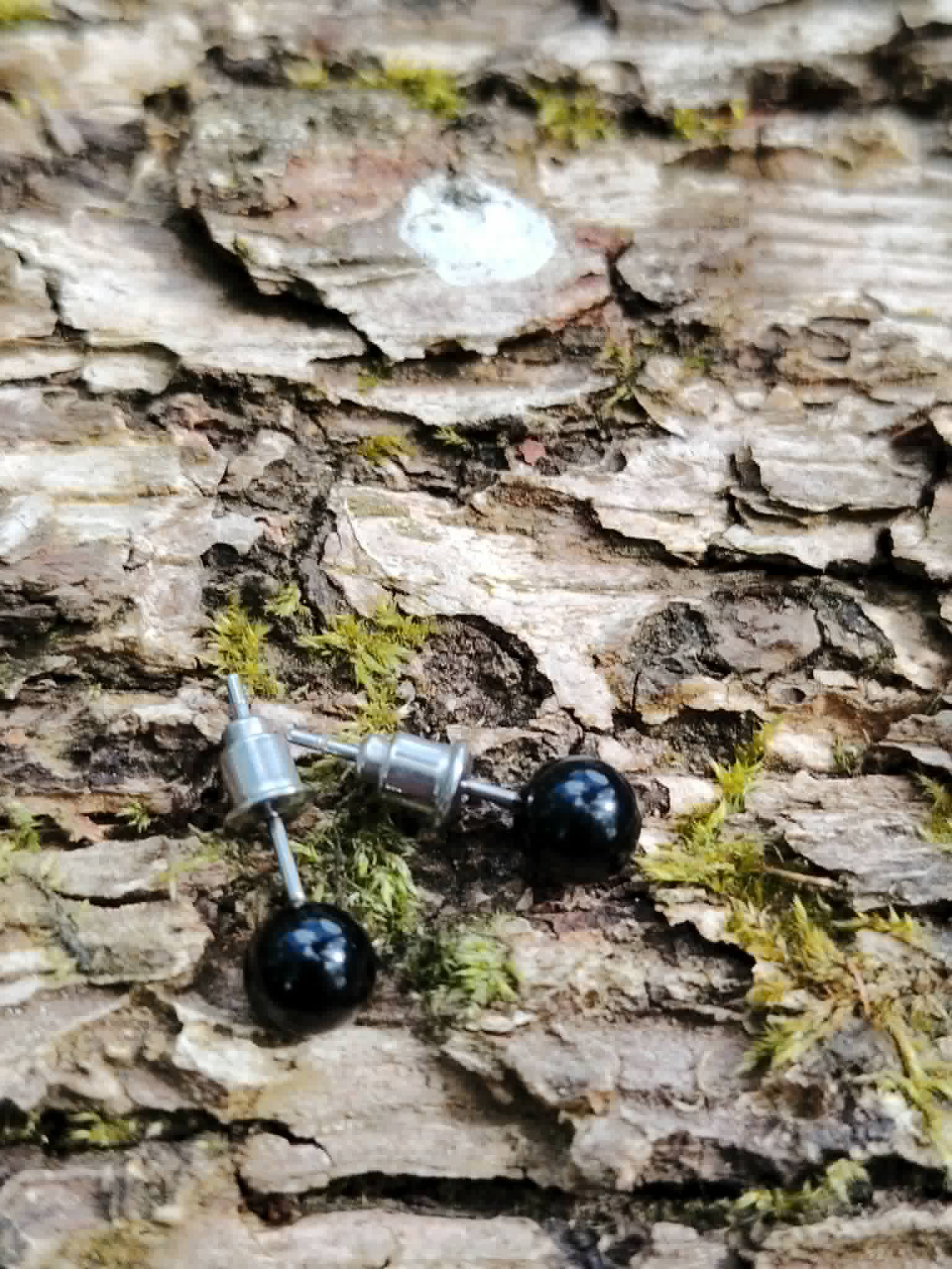 Boucles d’oreilles puces Obsidienne noire posées sur écorce moussue, pierre noire polie associée au recentrage et à l’ancrage.