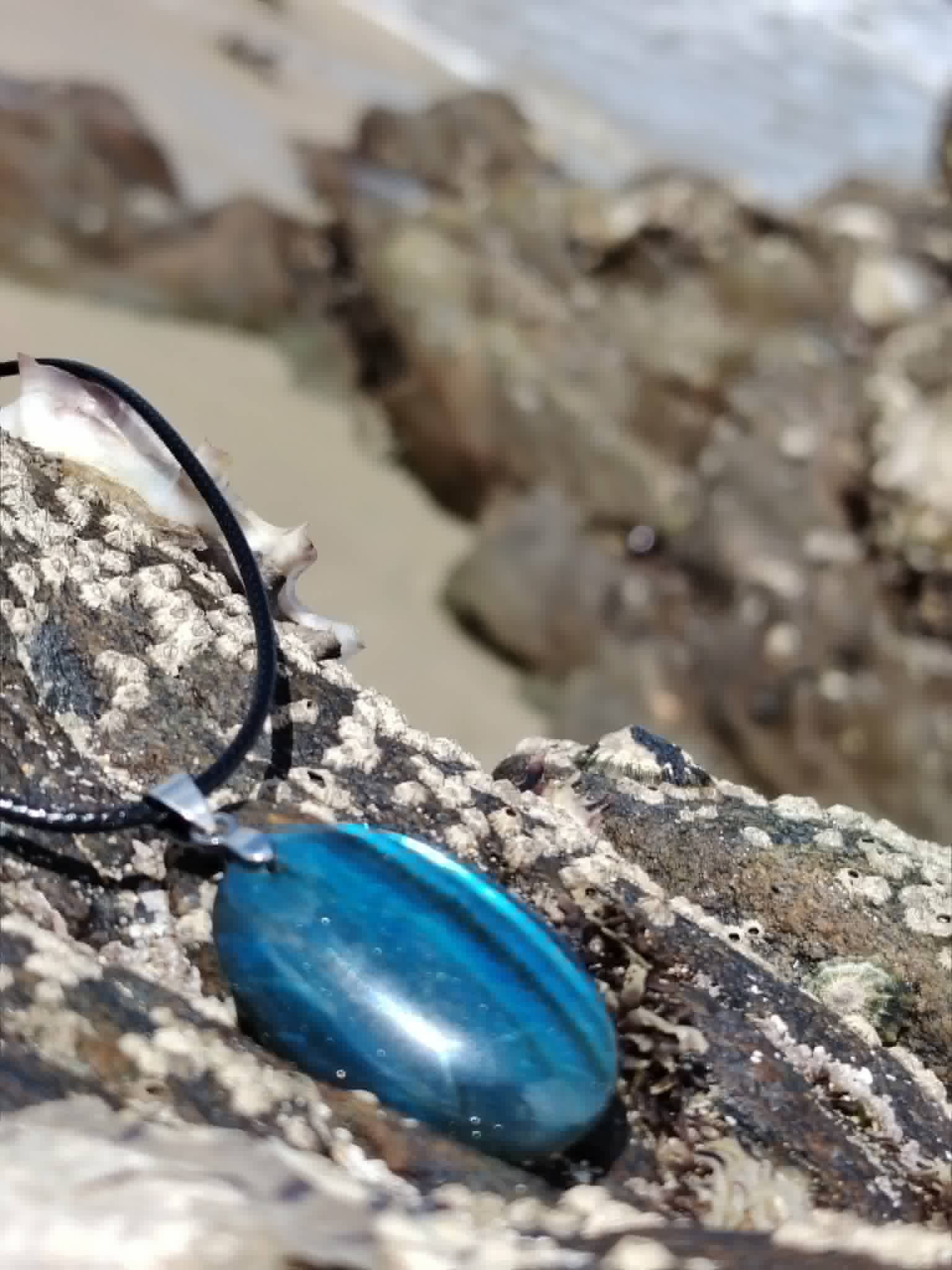 Pendentif Labradorite bleue allongé sur roche côtière en Bretagne, reflets bleus pour clarté mentale et protection.
