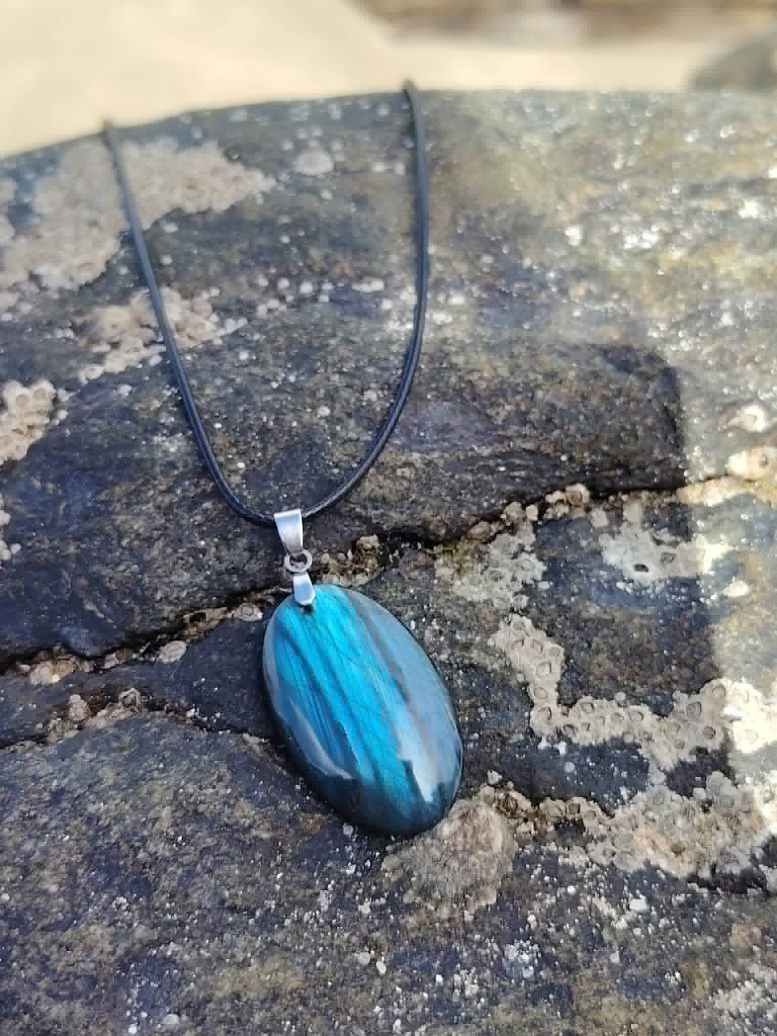 Pendentif Labradorite bleue sur pierre marine en Bretagne, cordon noir et bélière argentée pour harmonie subtile.