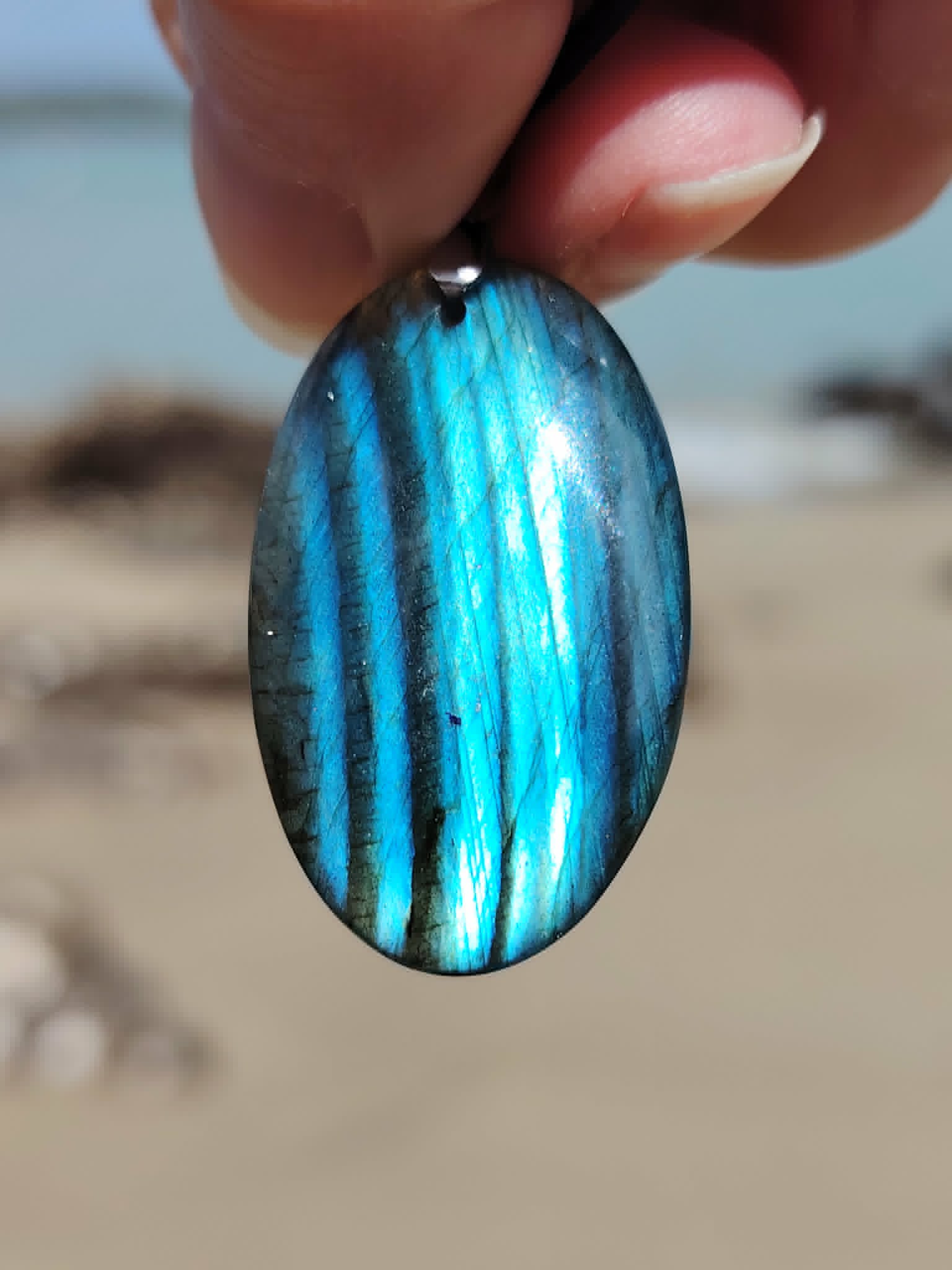 Labradorite bleue tenue devant la plage en Bretagne, pierre ovale brillante pour présence et perception subtile.