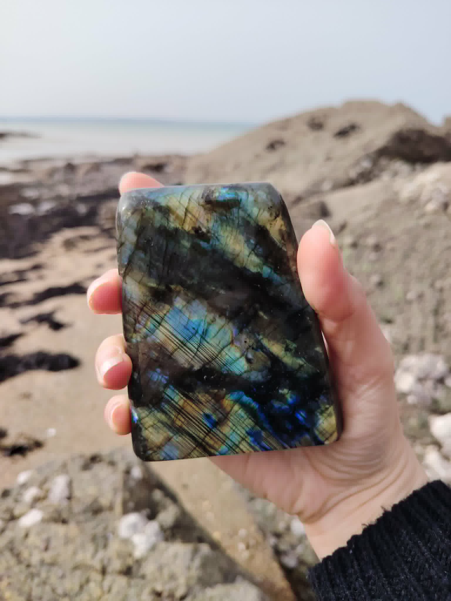 Labradorite forme libre tenue face à la mer en Bretagne, reflets boréals pour clarté mentale et apaisement intérieur.