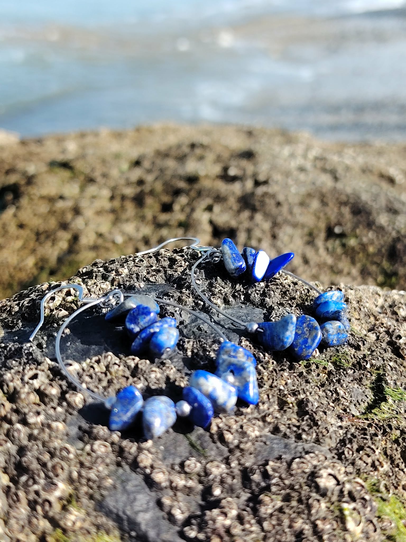 Création Magic Gaïa en Lapis-Lazuli posée sur roche bretonne, anneaux fins argentés et éclats bleus pour communication et clarté.