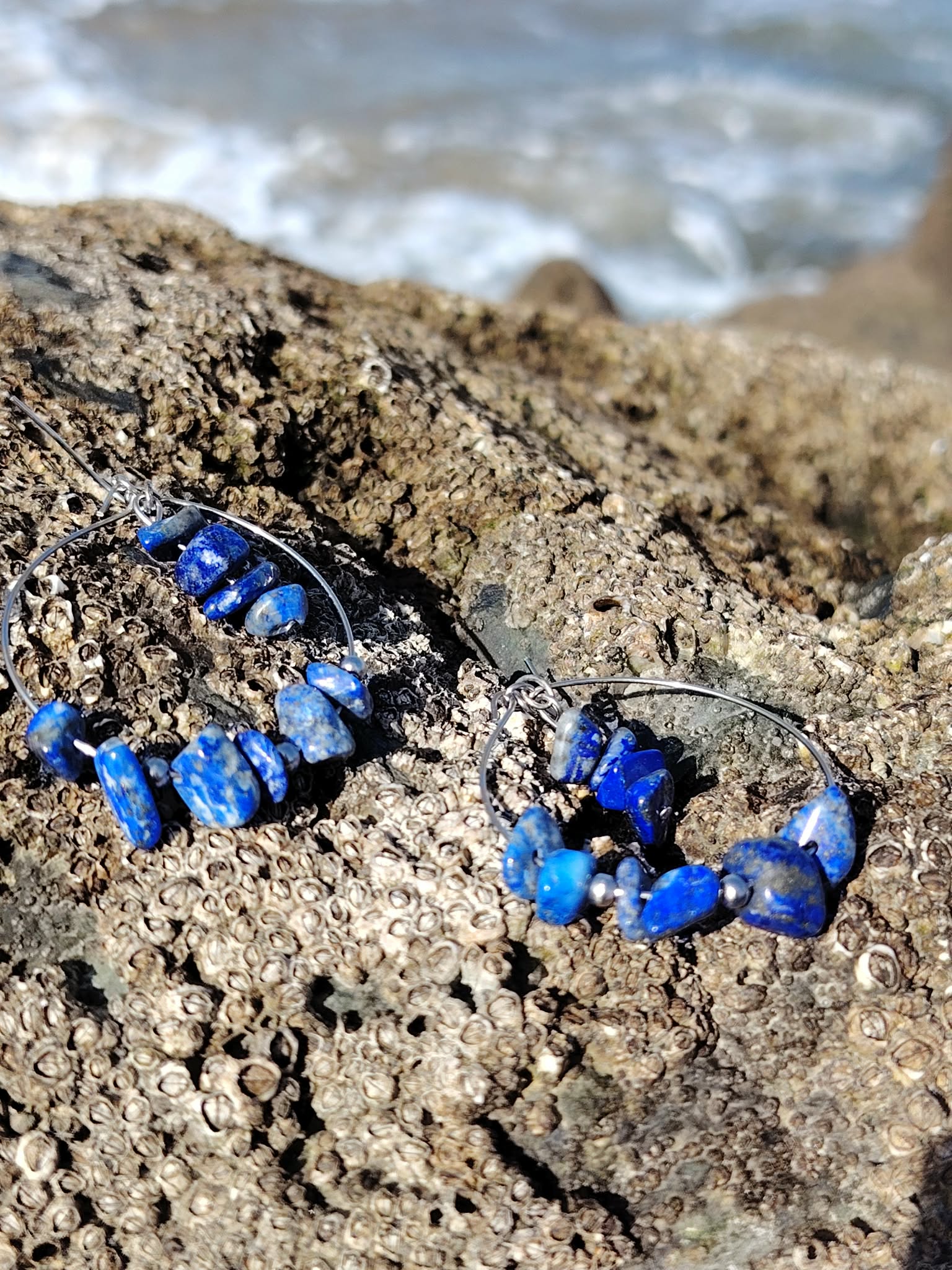 Vue rapprochée des boucles d’oreilles Lapis-Lazuli sur pierre marine en Bretagne, montage créatif avec chips bleues non régulières.