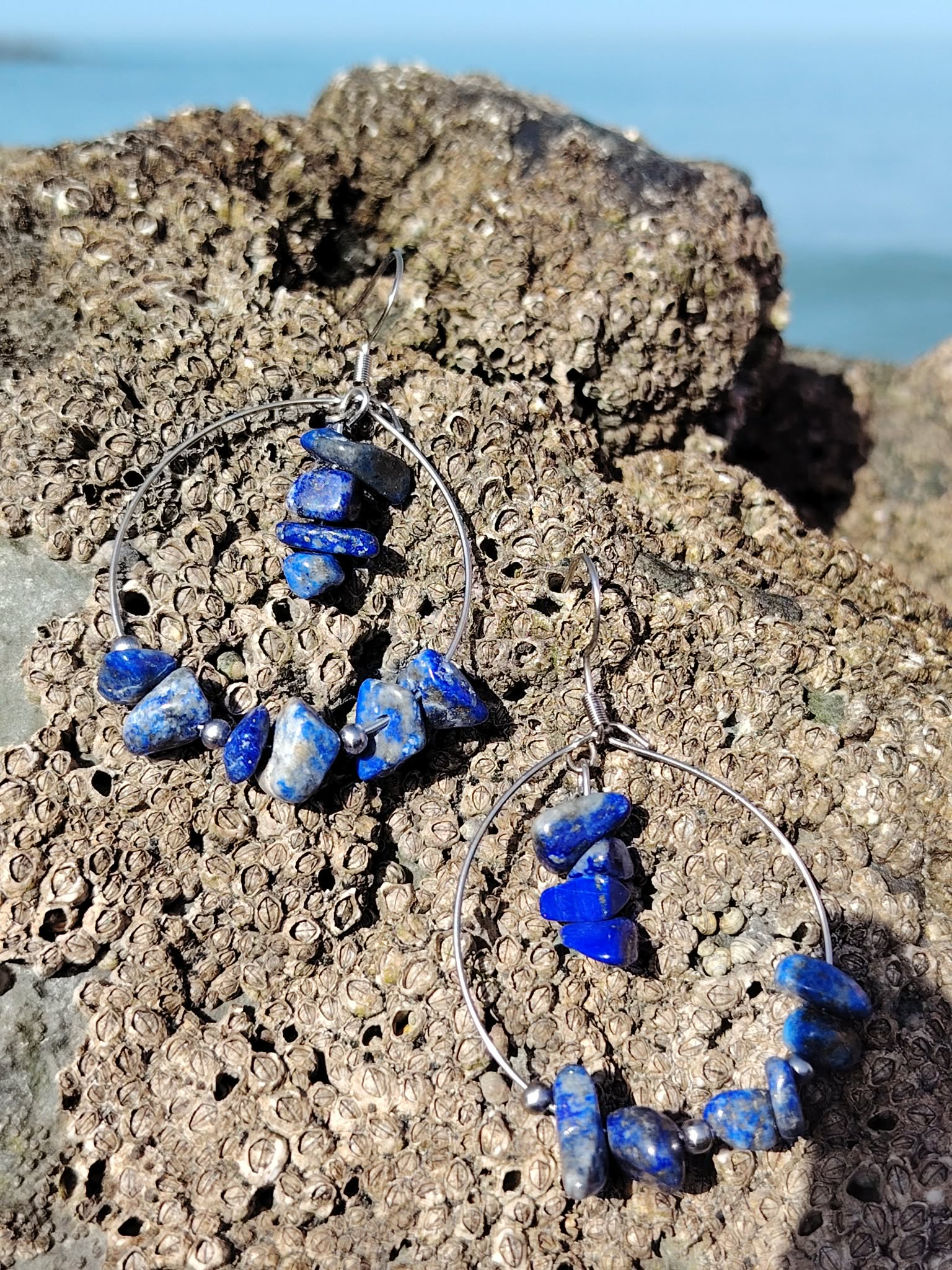 Boucles d’oreilles Lapis-Lazuli création Magic Gaïa sur rocher coquillé en bord de mer breton, pierres chips bleues irrégulières.