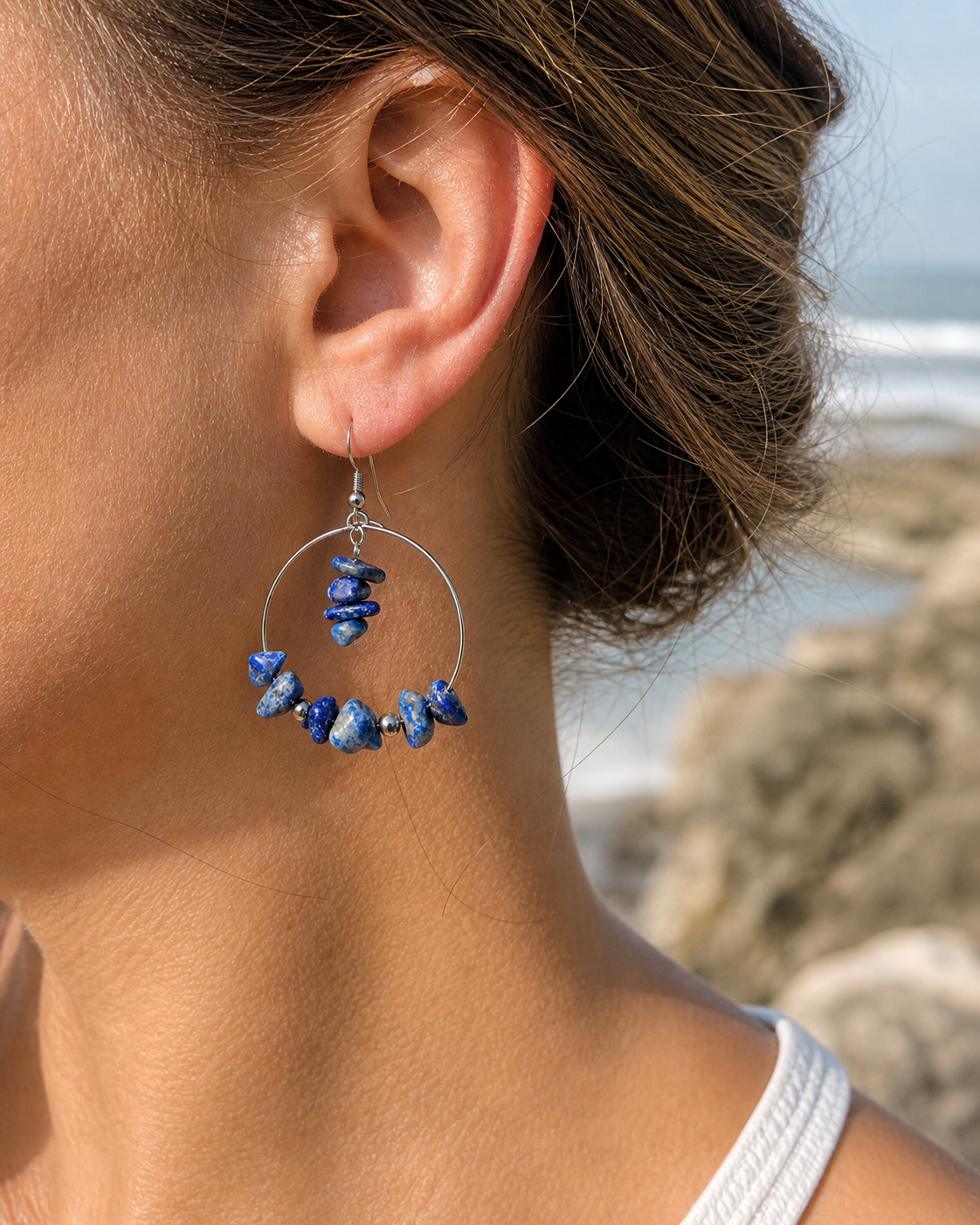 Boucle d’oreille Lapis-Lazuli création Magic Gaïa portée à l’oreille, fond marin flouté en Bretagne, chips bleues et acier inoxydable.