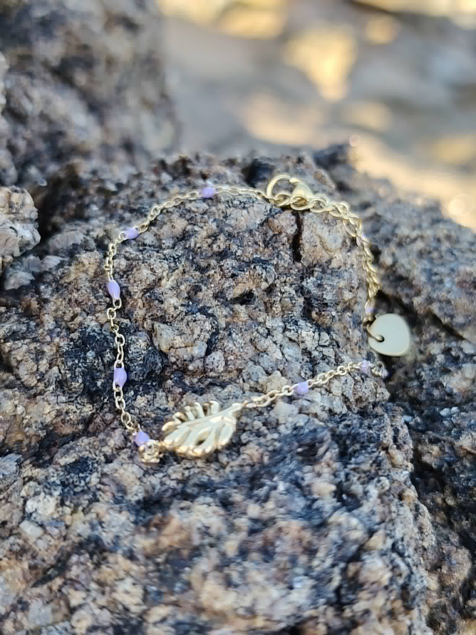 Bracelet Améthyste feuille dorée sur rocher breton en lumière douce, perles violettes facettées et acier inoxydable pour recentrage, lâcher prise et spiritualité.