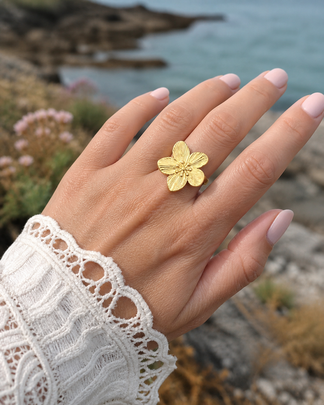 Bague fleur dorée réglable portée à la main près de la mer, acier inoxydable finition or 18K avec motif floral élégant et naturel.