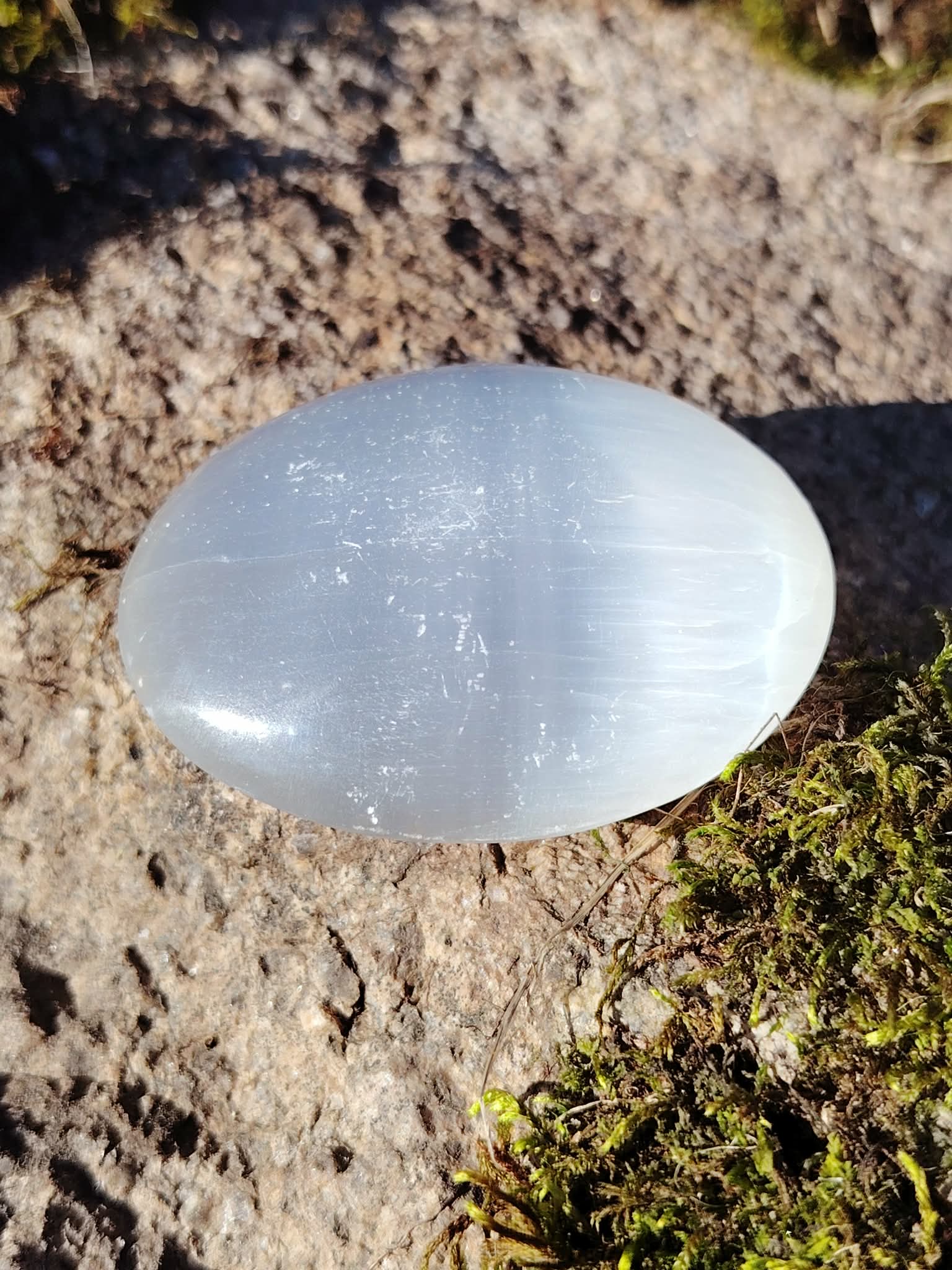 Galet blanc de Sélénite en gros plan sur rocher, texture satinée et éclat minéral pour douceur, repos mental et énergie claire.