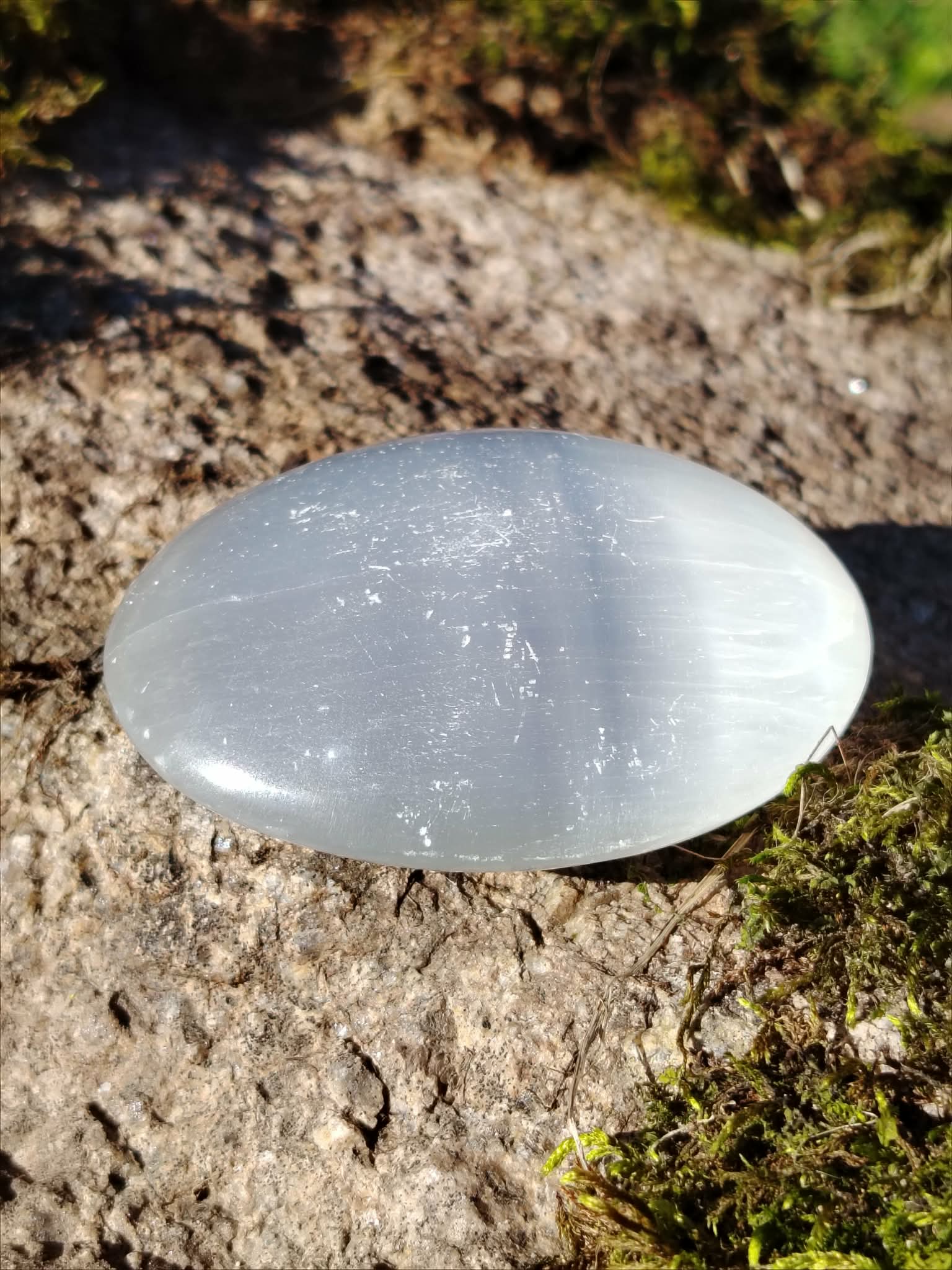 Galet Sélénite blanc laiteux sur pierre naturelle, forme ovale brillante avec fines stries visibles pour lumière et sérénité.