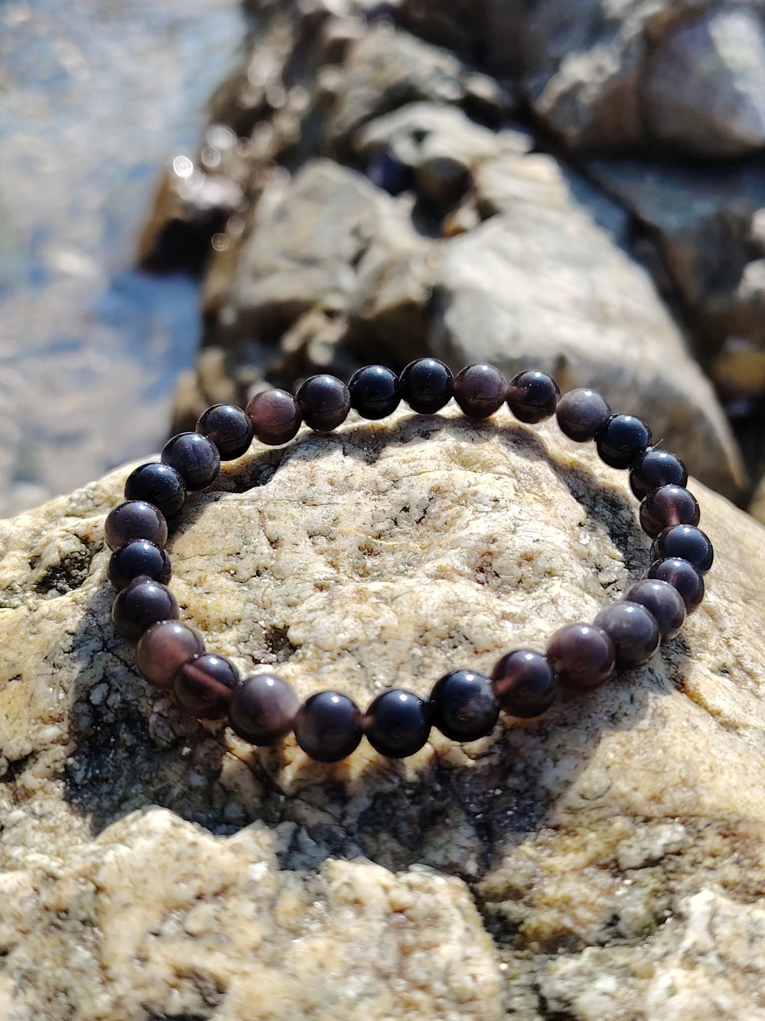Bracelet Obsidienne Argentée 6 mm posé sur un rocher en bord de mer en Bretagne, perles sombres aux reflets métallisés pour protection profonde.