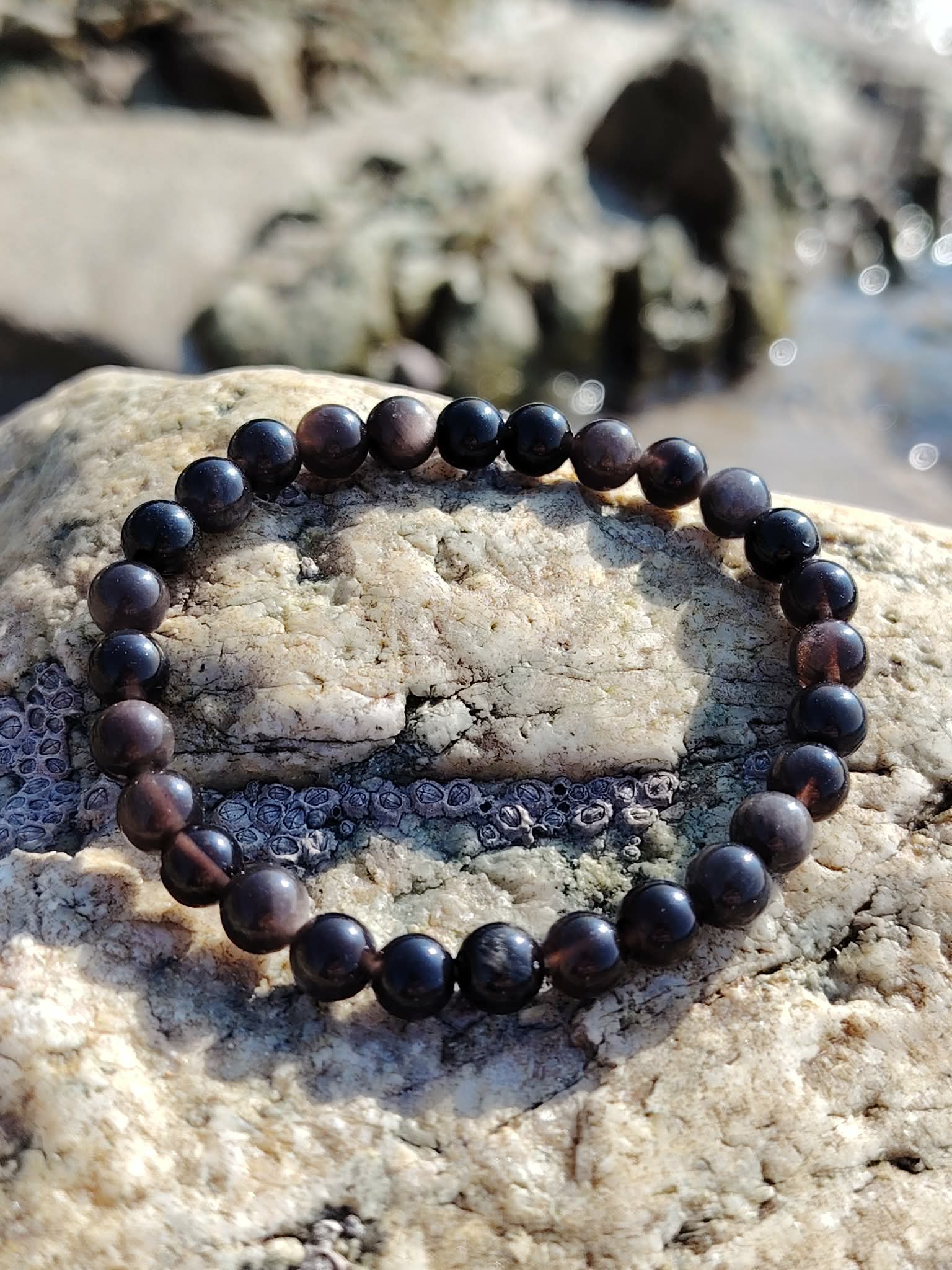 Bracelet en Obsidienne Argentée sur pierre claire au bord de l’eau, reflets gris argentés pour accompagner vérité intérieure et maîtrise de soi.