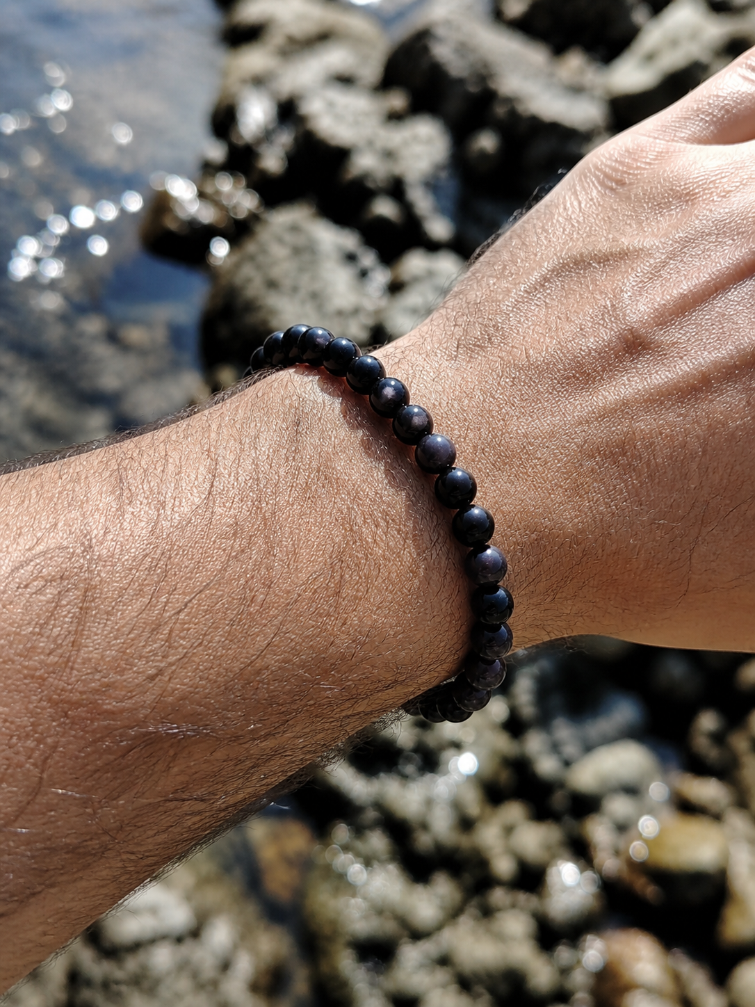 Bracelet Obsidienne Argentée porté au poignet près des rochers bretons, bijou en pierre naturelle associé à l’ancrage et à la stabilité émotionnelle.