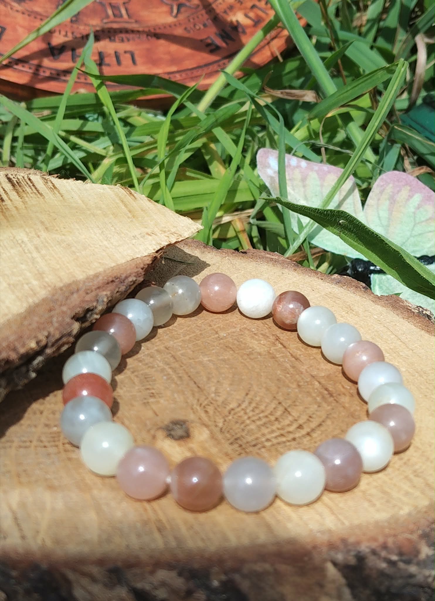 Bracelet Pierre de Lune beige multicolore sur tranche de bois au soleil, bijou naturel aux tons pêche, blanc et gris pour douceur lunaire.