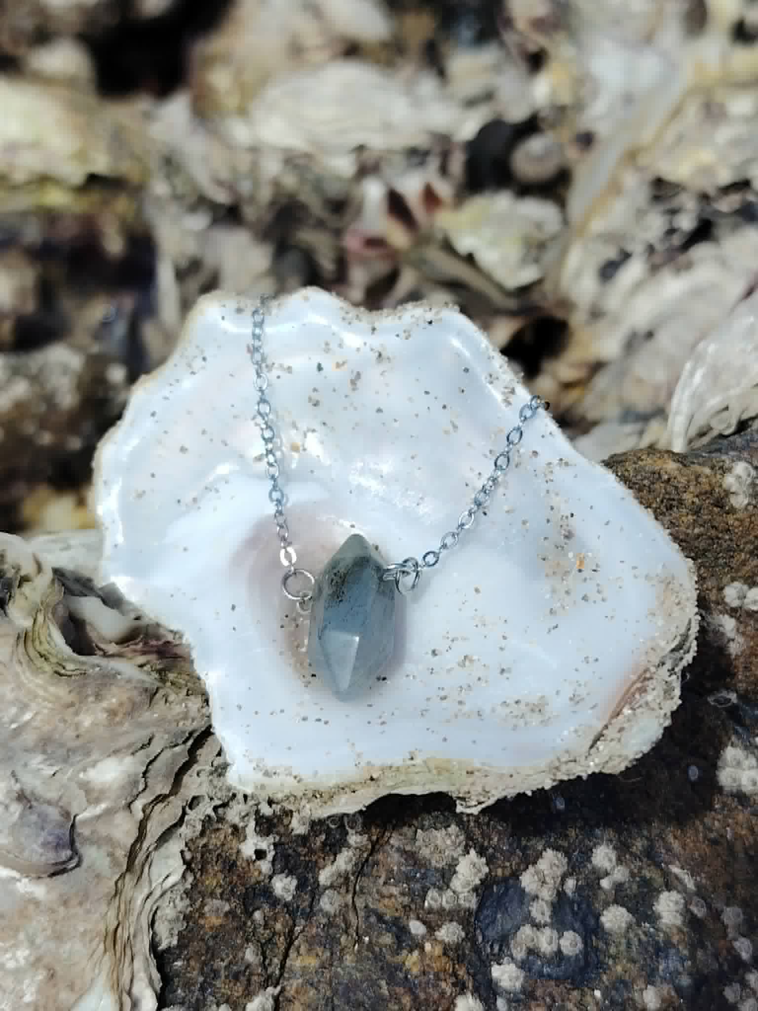 Pendentif Labradorite en forme de pointe posé dans une coquille blanche, pierre minérale grisée pour clarté intérieure et équilibre énergétique.