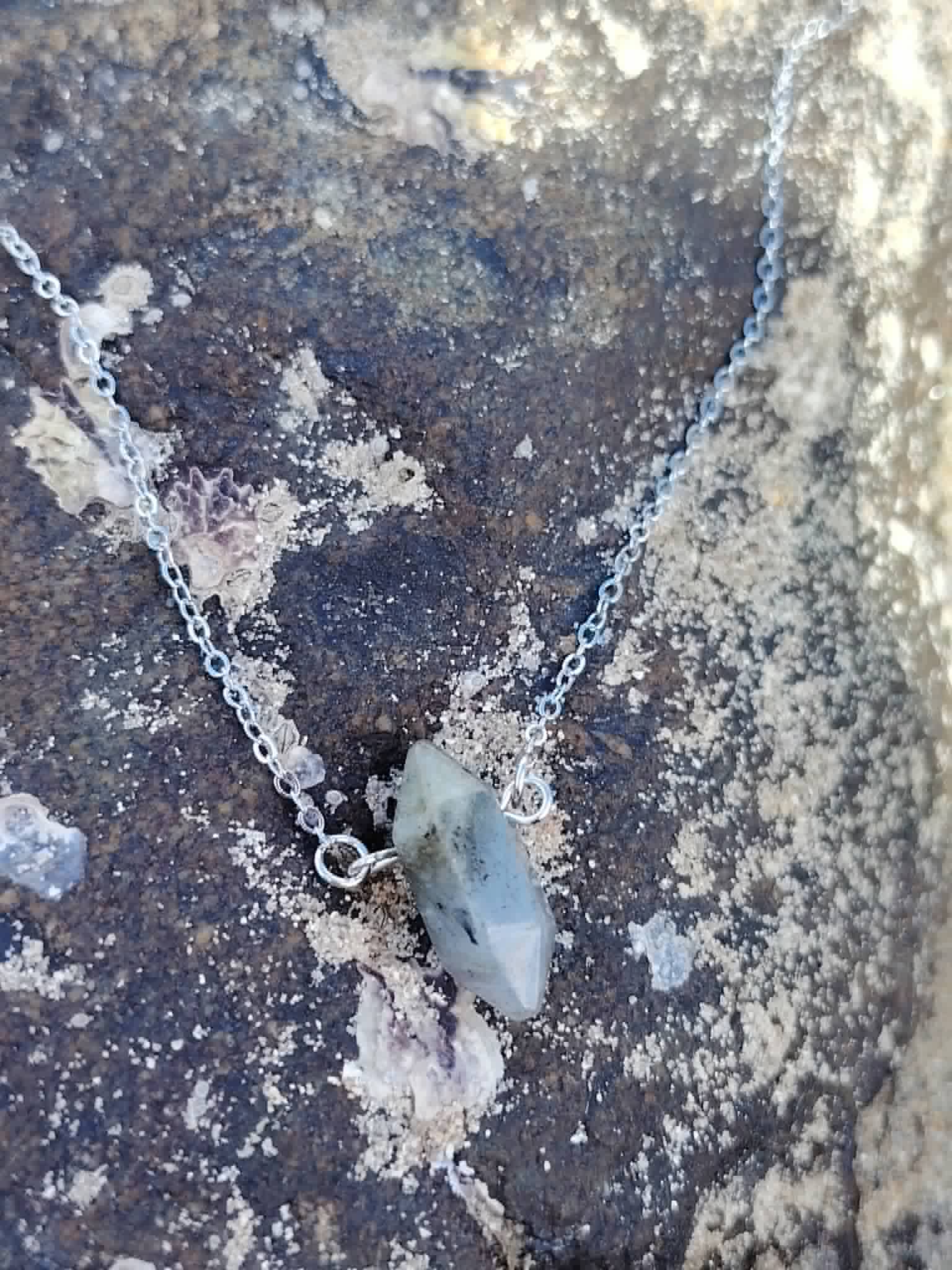Pendentif Labradorite sur roche côtière, pointe gris clair avec inclusions noires et chaîne fine pour protection symbolique et recentrage.